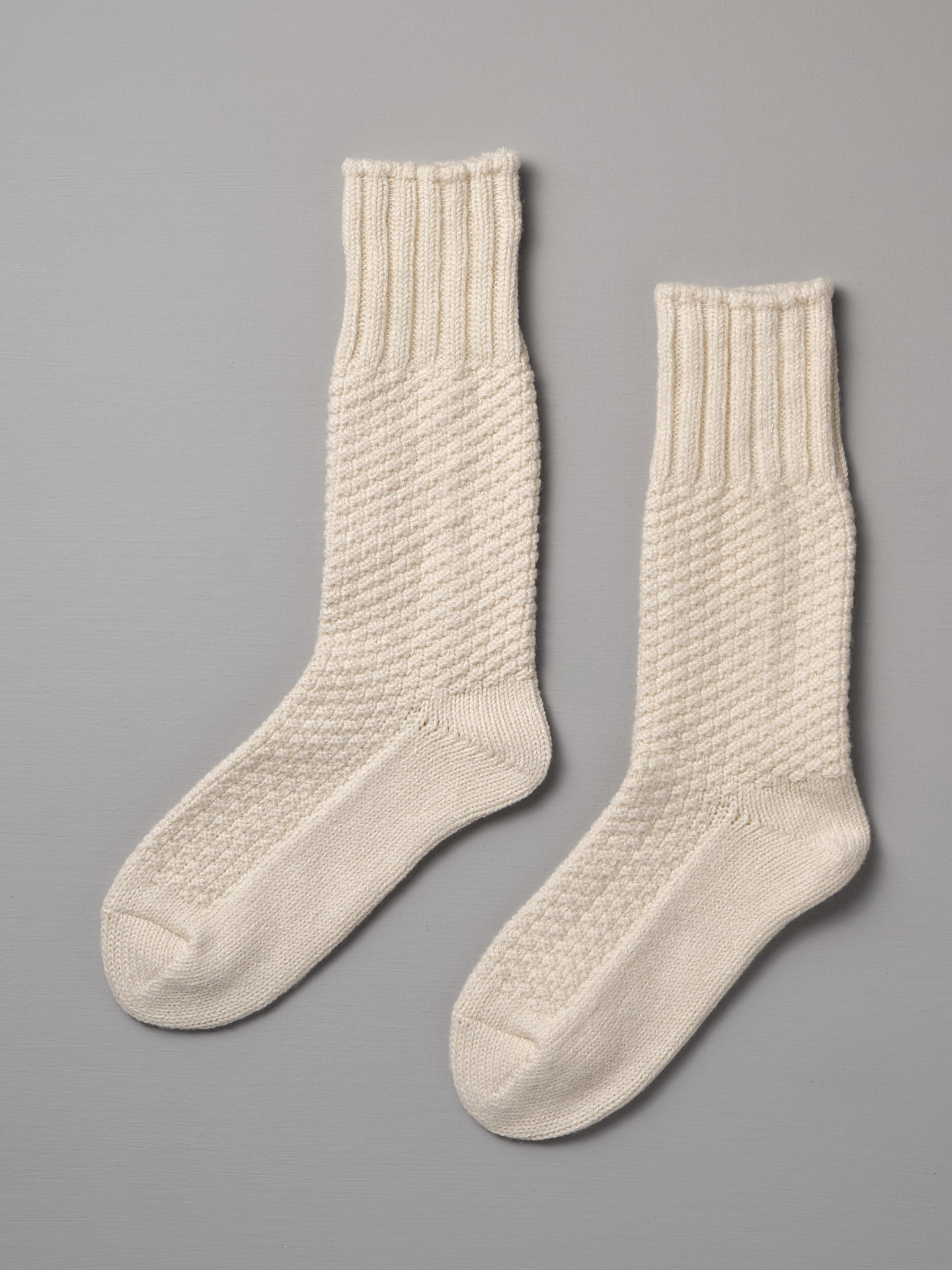 A pair of Nishiguchi Kutsushita Wool Cotton Boot Socks – Ivory with ribbed cuffs and a textured pattern on a gray background, available in Men's US and Women's US sizes.
