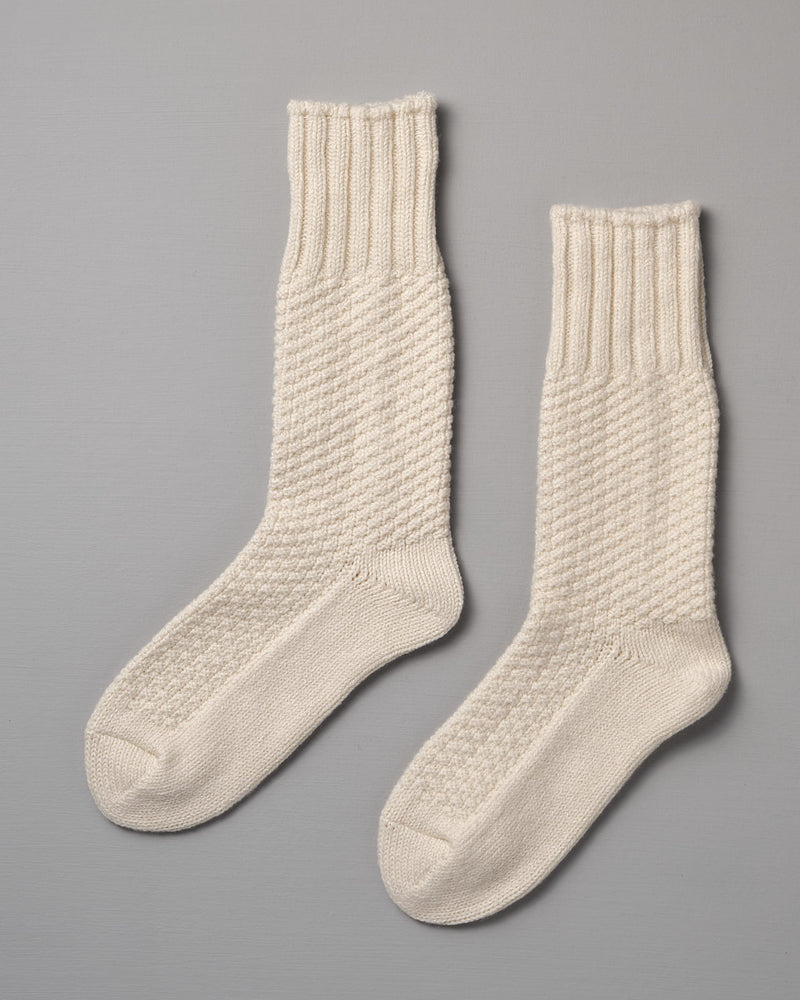 A pair of Nishiguchi Kutsushita Wool Cotton Boot Socks – Ivory with ribbed cuffs and a textured pattern on a gray background, available in Men's US and Women's US sizes.