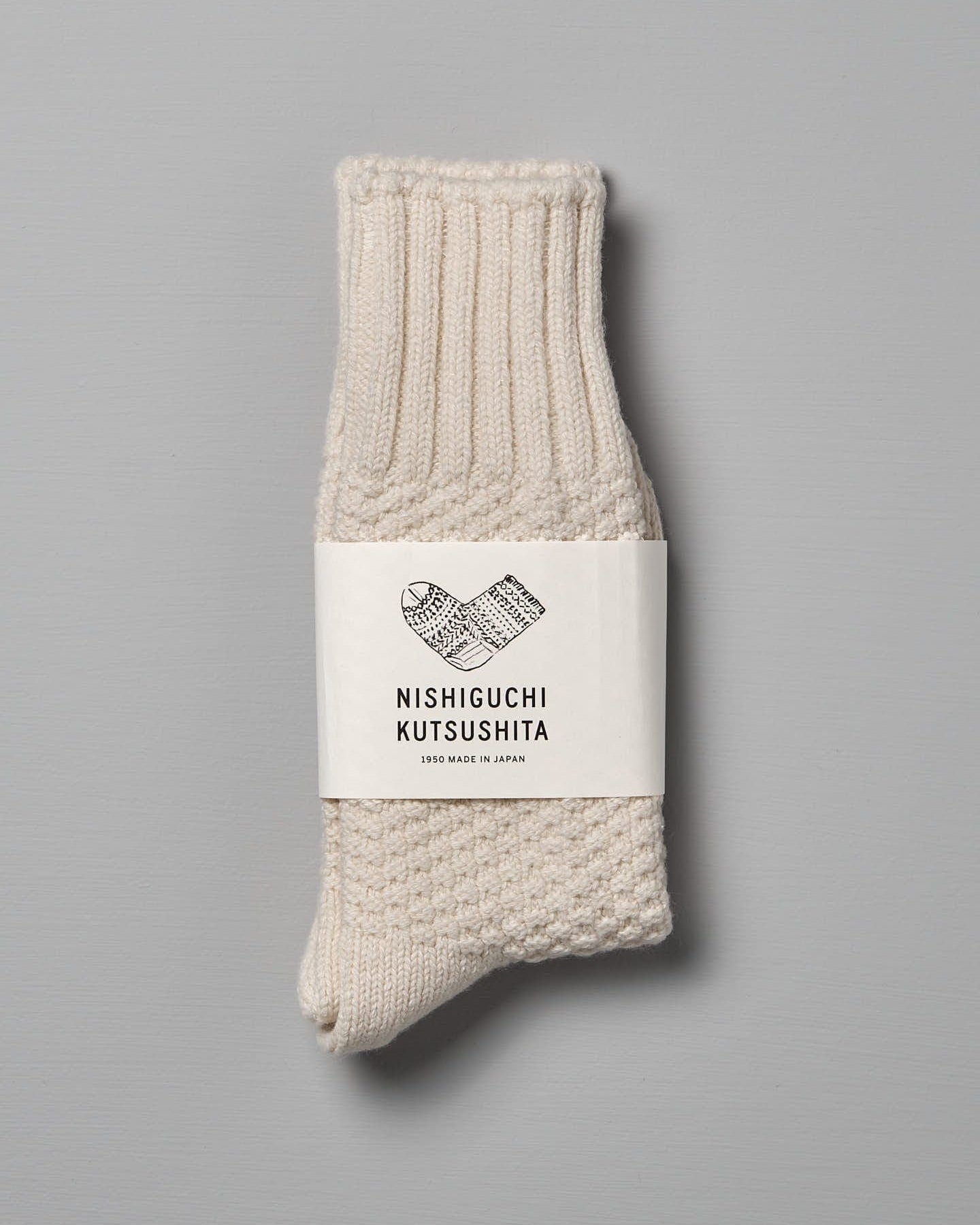 A pair of Nishiguchi Kutsushita Wool Cotton Boot Socks – Ivory with ribbed cuffs and a textured pattern on a gray background, available in Men's US and Women's US sizes.