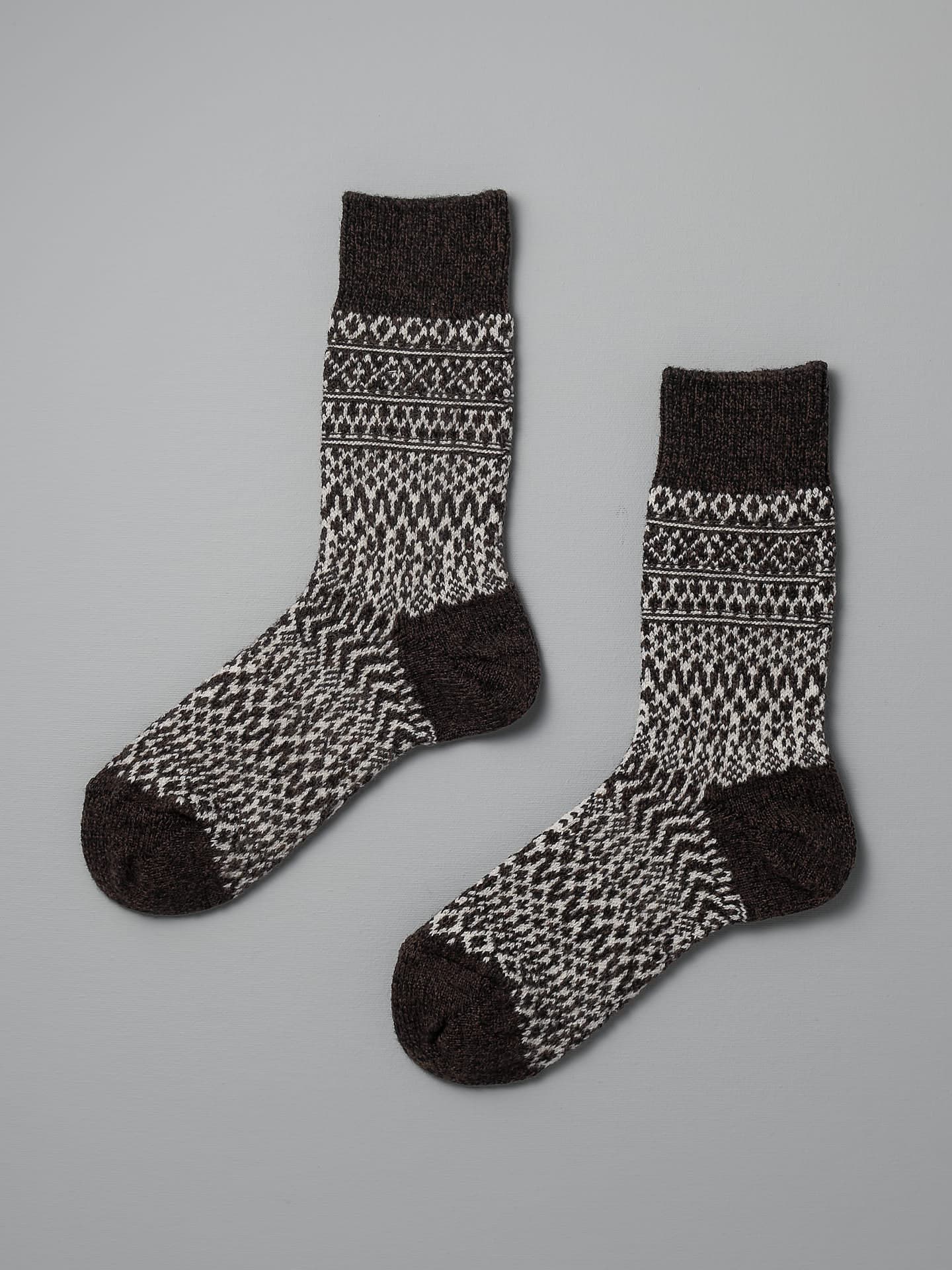 A pair of Oslo Wool Jacquard Socks – Coffee by Nishiguchi Kutsushita with geometric patterns, laying flat on a gray background. Check the size chart for EUR, UK, US conversion to ensure they fit perfectly.