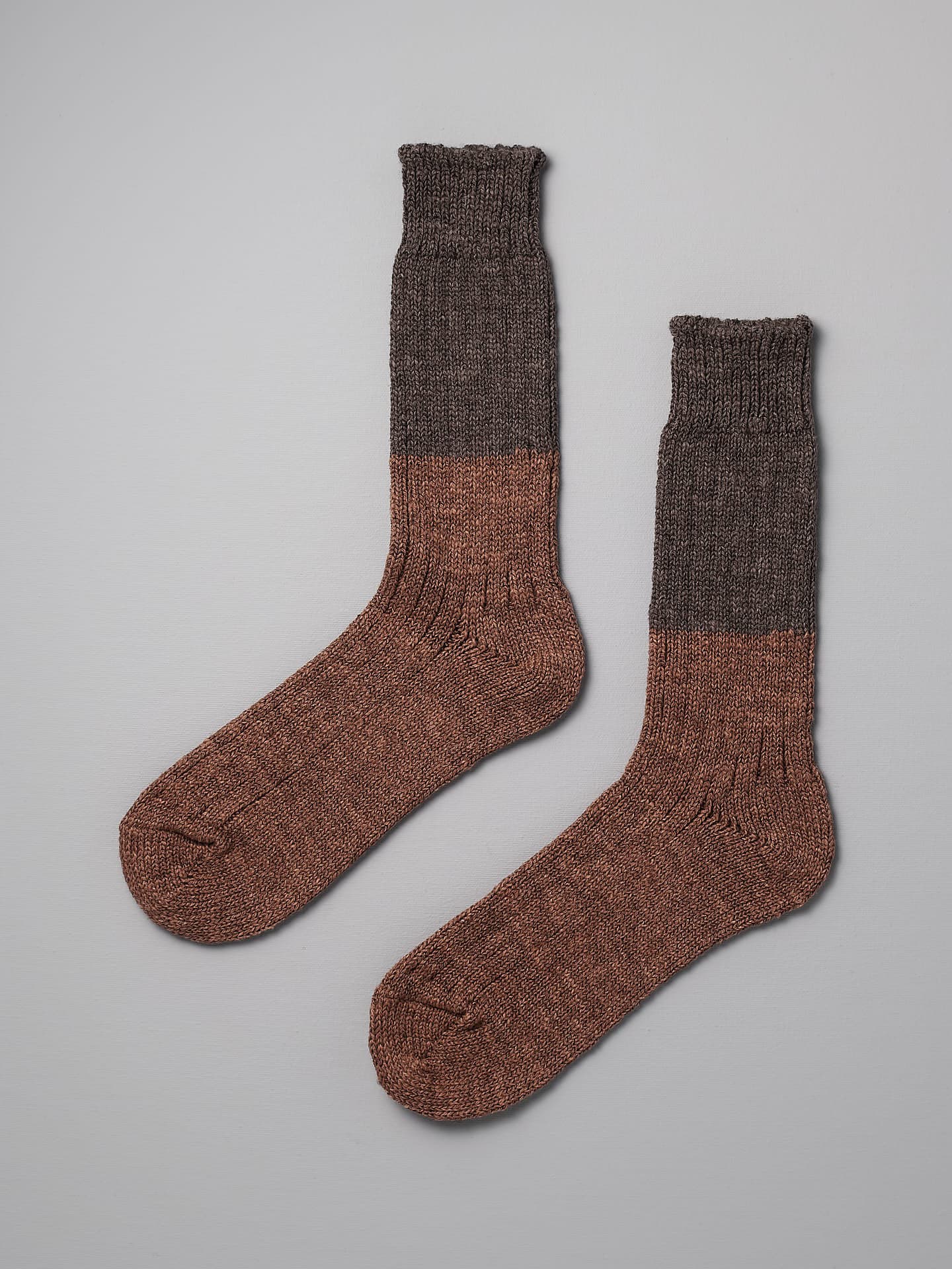 Two Nishiguchi Kutsushita Boston Slab Socks – Brown Fawn with a two-tone design, featuring a darker brown color above the ankle and a lighter brown color covering the foot and lower calf, are laid flat on a light grey surface. Available in both men's and women's shoe sizes, they correspond to the EUR and US size charts.