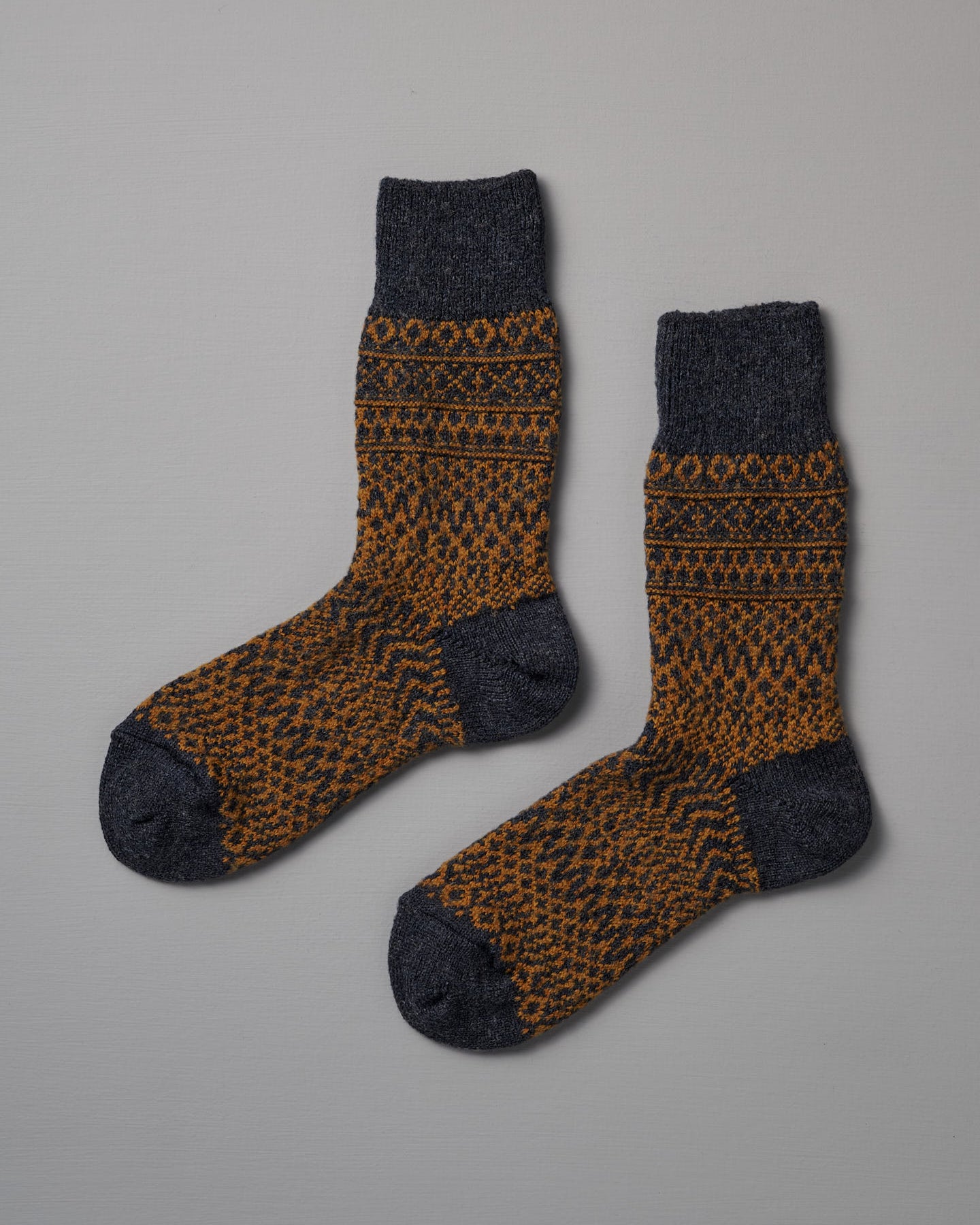 Nishiguchi Kutsushita’s Oslo Wool Jacquard Socks – Navy feature dark gray toes, heels, and cuffs with an orange and dark gray geometric pattern. Check our size chart to find your perfect fit.
