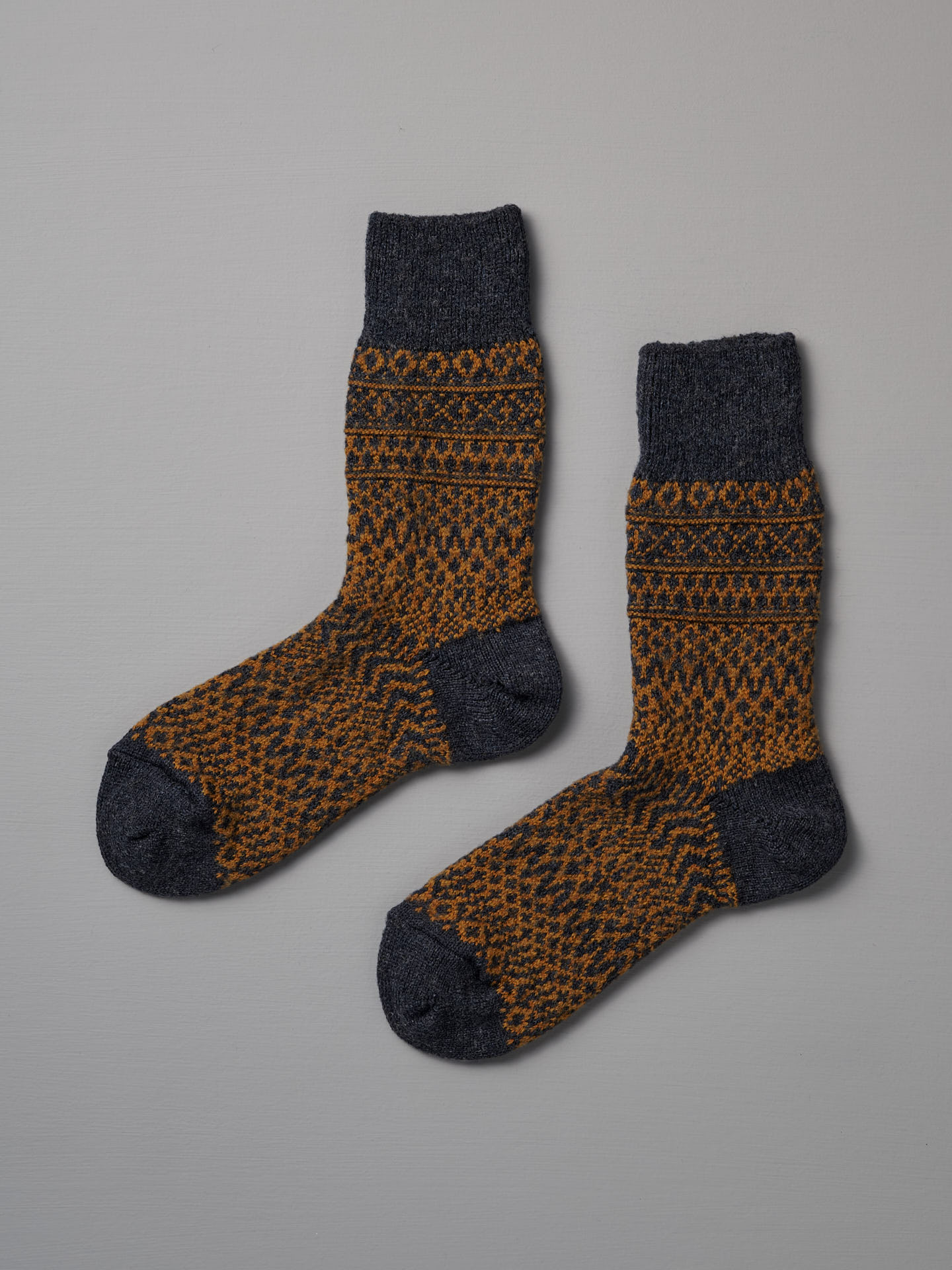 Nishiguchi Kutsushita’s Oslo Wool Jacquard Socks – Navy feature dark gray toes, heels, and cuffs with an orange and dark gray geometric pattern. Check our size chart to find your perfect fit.