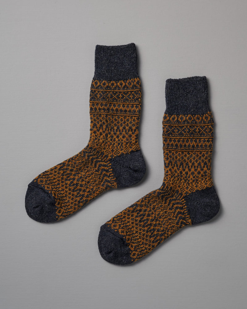 Nishiguchi Kutsushita’s Oslo Wool Jacquard Socks – Navy feature dark gray toes, heels, and cuffs with an orange and dark gray geometric pattern. Check our size chart to find your perfect fit.