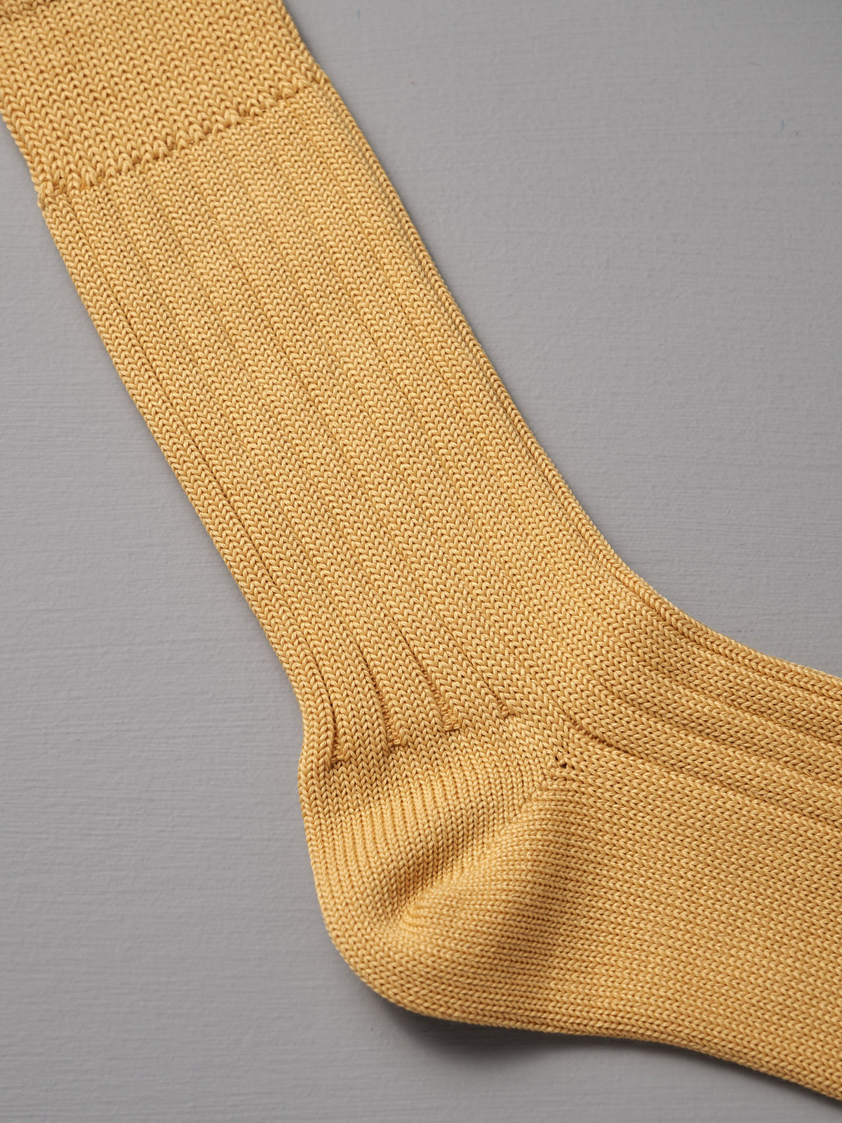 A close-up of a single Praha Cotton Sock – Susuki-Gold by Nishiguchi Kutsushita, shown on a flat grey surface.