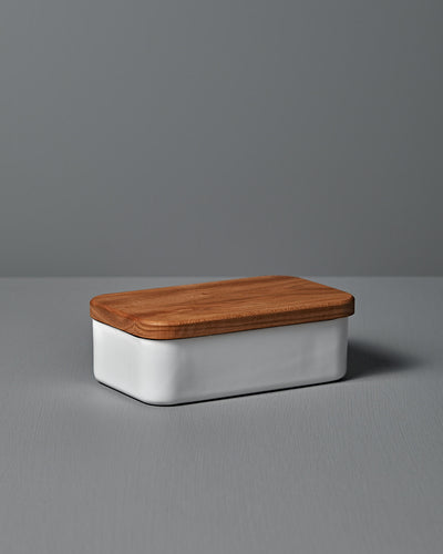 The Noda Horo Enamel Butter Case – 200g, with its sleek white ceramic body and cherry wood lid, rests elegantly on a gray surface, providing stylish food storage.