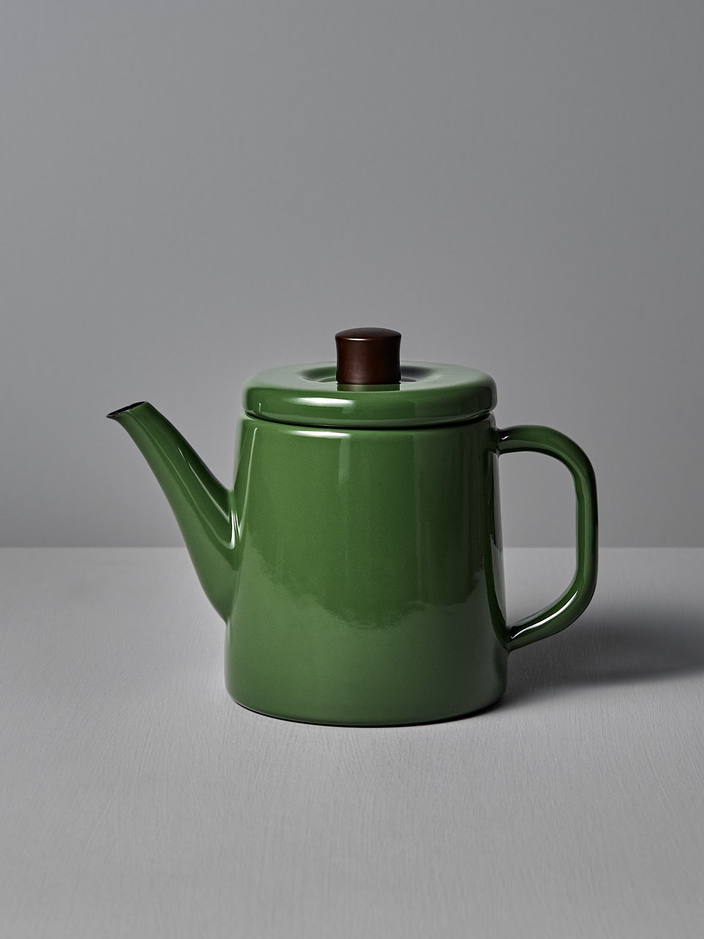 A Noda Horo Potoru Stove-top Kettle/Teapot in green, featuring a brown wooden lid handle and inspired by traditional Japanese design, is set against a gray background on a plain surface.