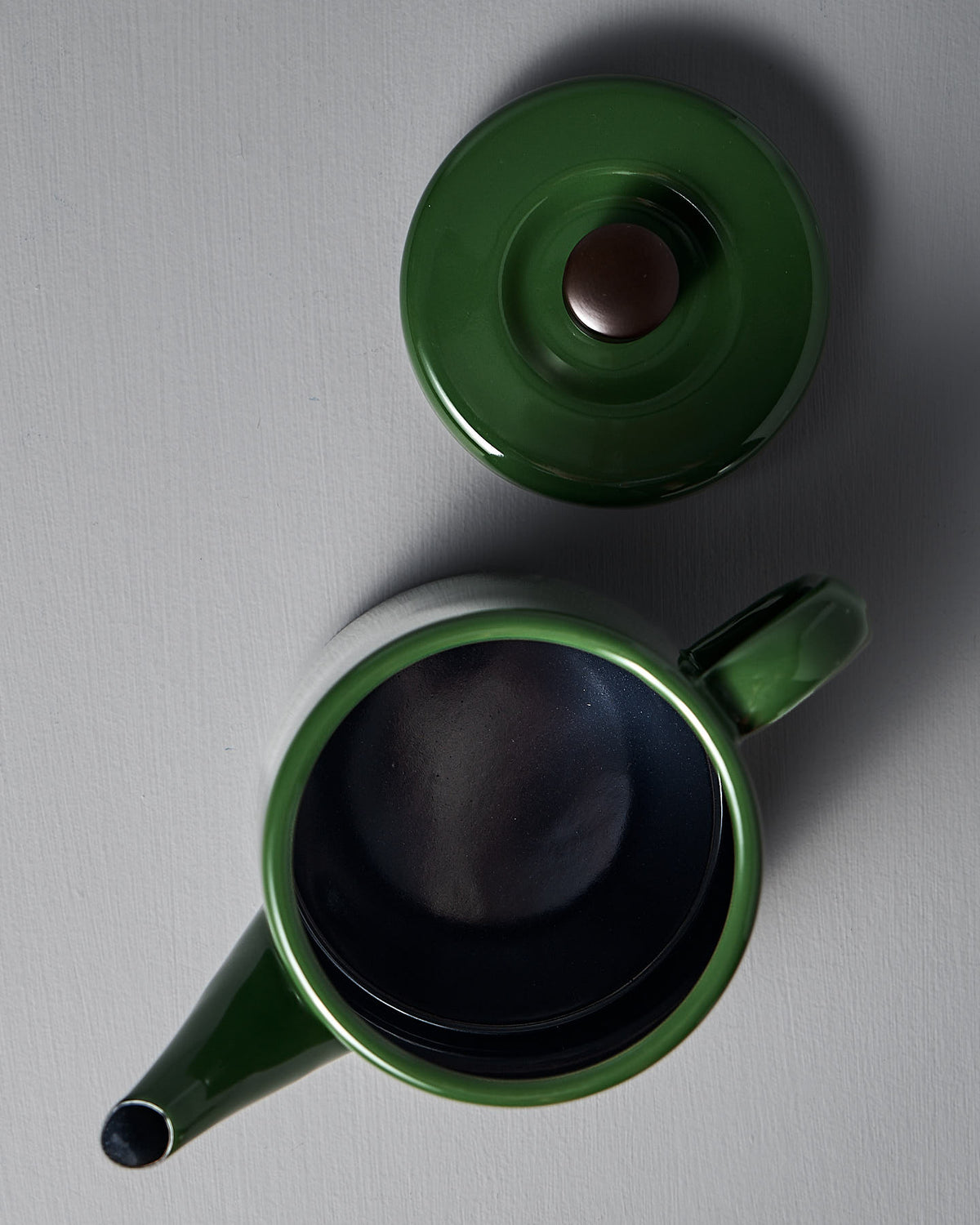 Seen from above, the Potoru Stove-top Kettle/Teapot by Noda Horo, exuding Japanese kitchenware charm in its green ceramic design, rests on a flat surface with its lid removed.