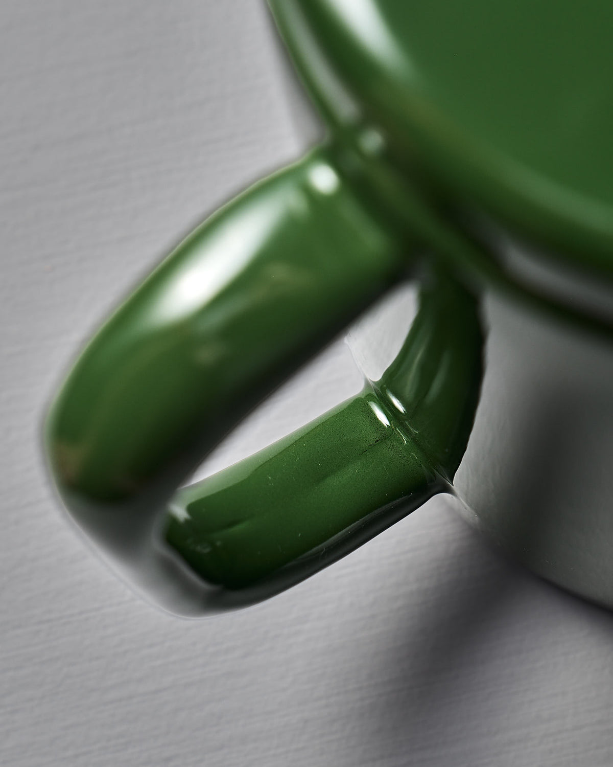A close-up of the Potoru Stove-top Kettle/Teapot – Green (Noda Horo) reveals its glossy handle on a white surface, reminiscent of fine Japanese kitchenware with smooth curves and a polished finish.