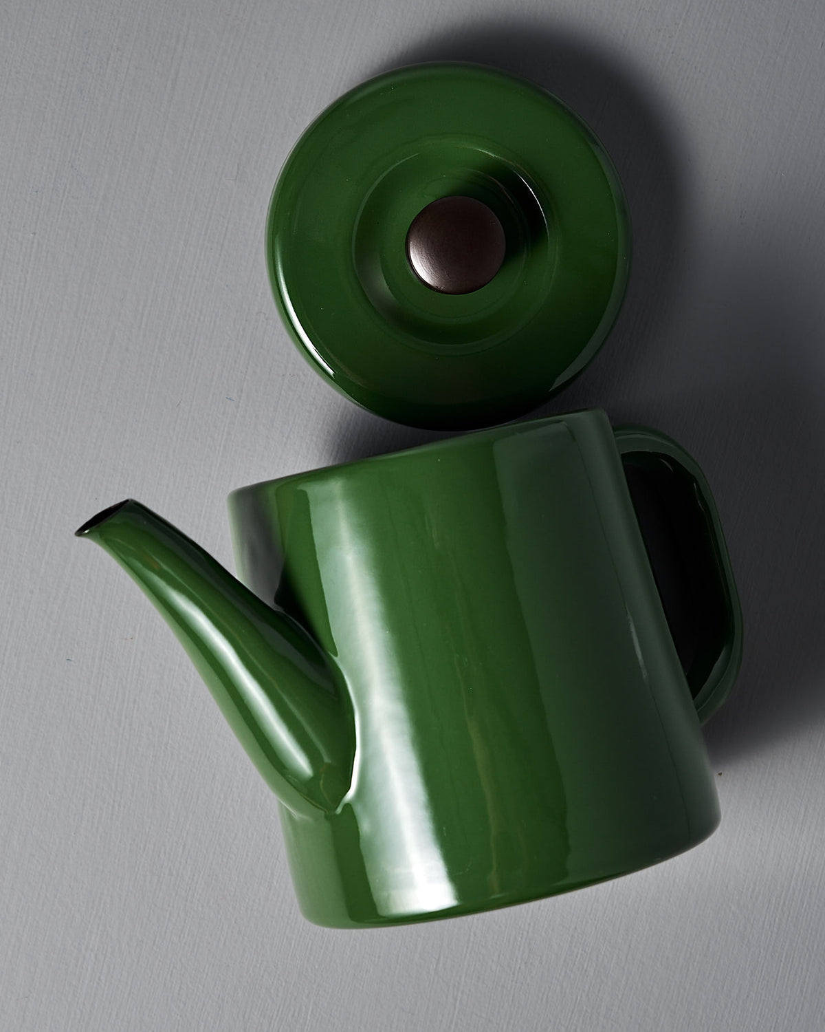 A Noda Horo Potoru stove-top kettle/teapot in green ceramic with a matching lid rests elegantly on a gray surface, adding traditional Japanese charm to any space.
