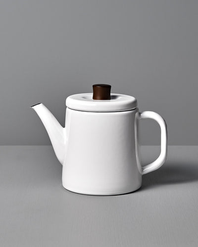 The Potoru Stove-top Kettle/Teapot – White, by Noda Horo, features a dark brown lid handle and is set elegantly on a gray surface against a gray backdrop, reminiscent of Japanese kitchenware.