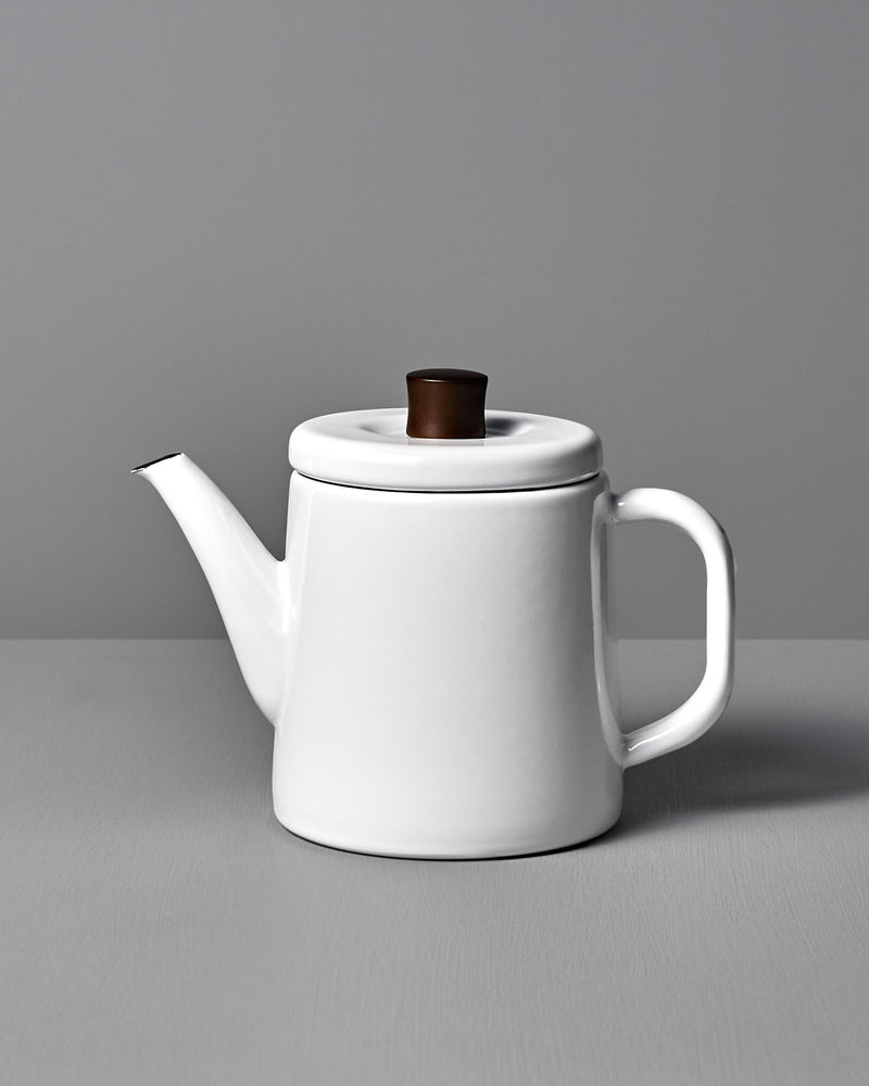 The Potoru Stove-top Kettle/Teapot – White, by Noda Horo, features a dark brown lid handle and is set elegantly on a gray surface against a gray backdrop, reminiscent of Japanese kitchenware.