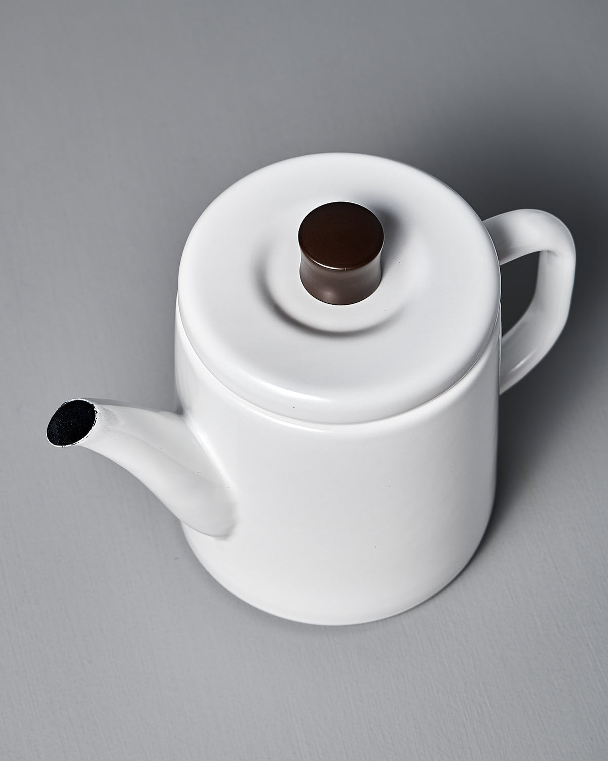 Noda Horo's Potoru Stove-top Kettle/Teapot in white, featuring a brown knob on the lid, elegantly captures the essence of Japanese kitchenware against a gray surface.
