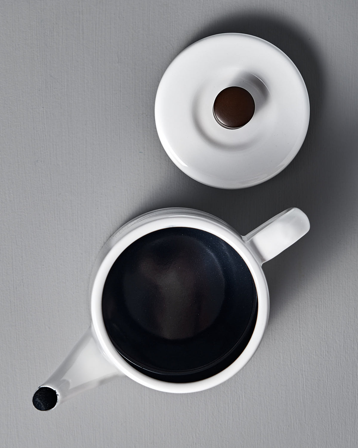 Aerial view of the Noda Horo Potoru Stove-top Kettle/Teapot in white, filled with brown liquid on a gray surface, with the lid ajar.