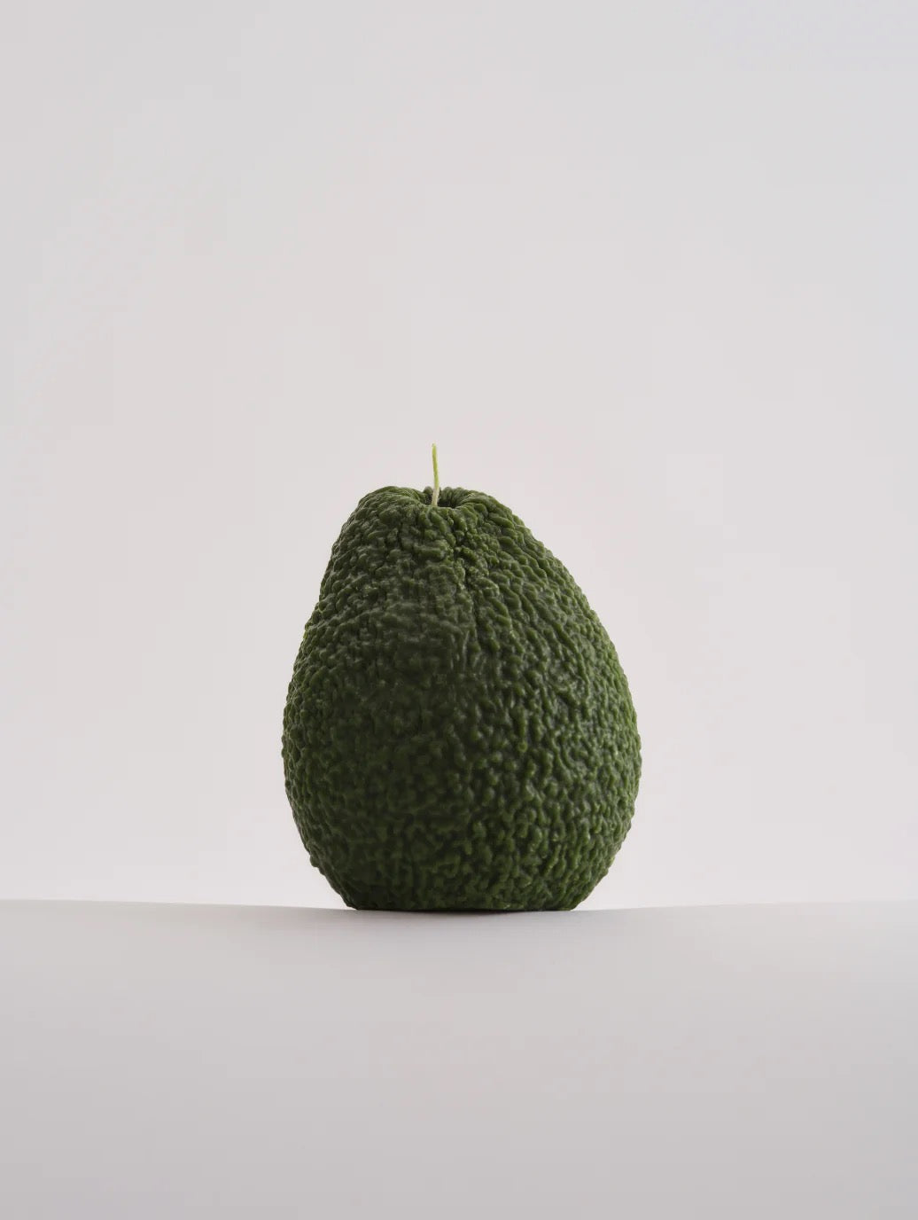 A hand-made Nonna&#39;s Grocer Avocado Candle – Small crafted from a soy wax blend, delicately placed on a white surface.