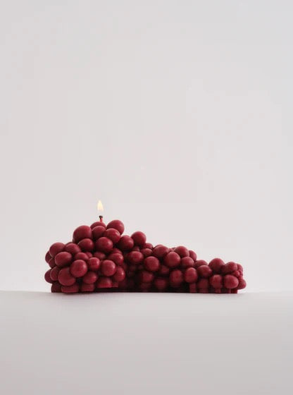 A hand-made Grapes Candle - Bordeaux from Nonna&#39;s Grocer is sitting on top of a bunch of red grapes.