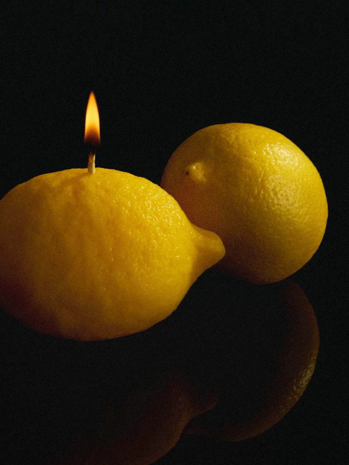 A Scented Lemon Candle by Nonna&#39;s Grocer glows softly against the dark background.