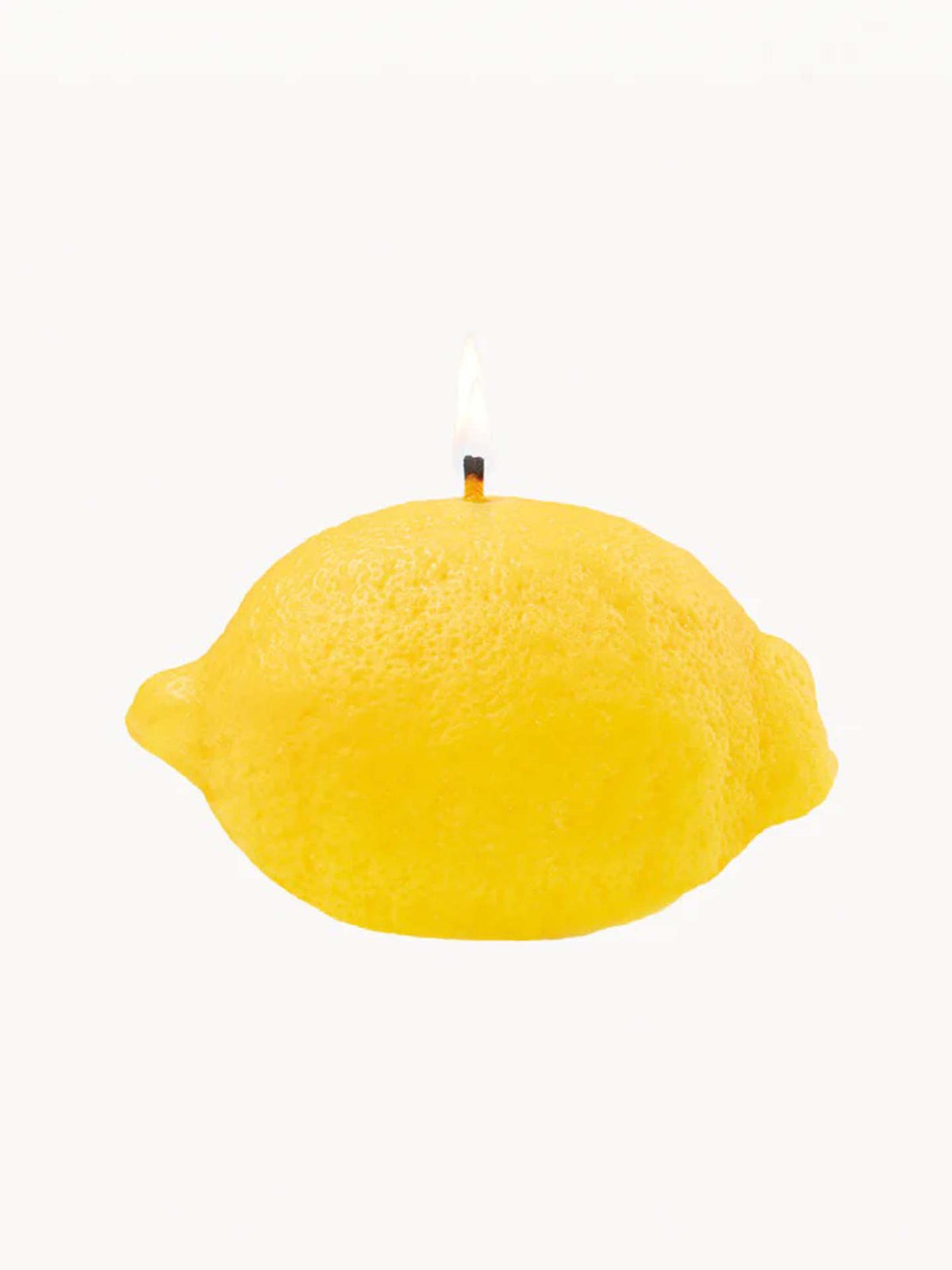 The Scented Lemon Candle by Nonna&#39;s Grocer is designed in the shape of a yellow lemon, featuring a lit wick on top and crafted from a natural soy wax blend.