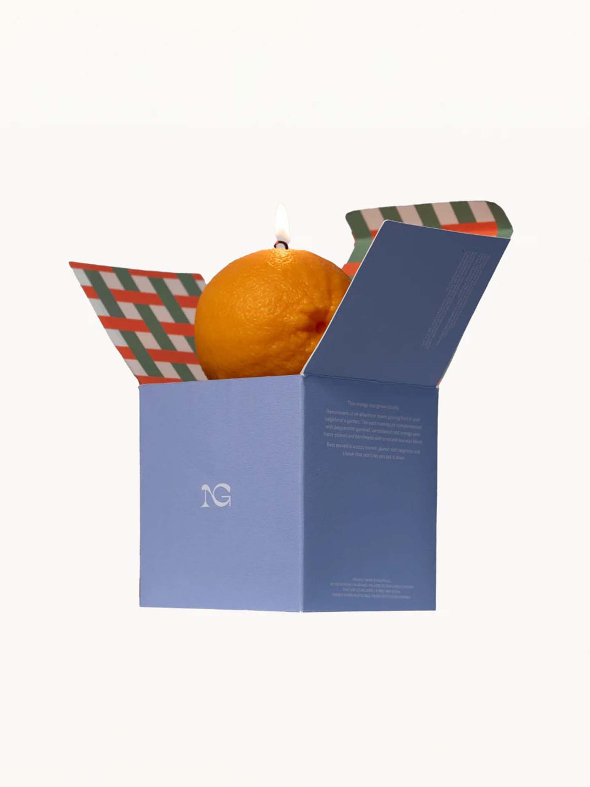 A Scented Orange Candle by Nonna&#39;s Grocer, crafted from natural soy wax, is lit and placed inside an opened blue box with a patterned interior.