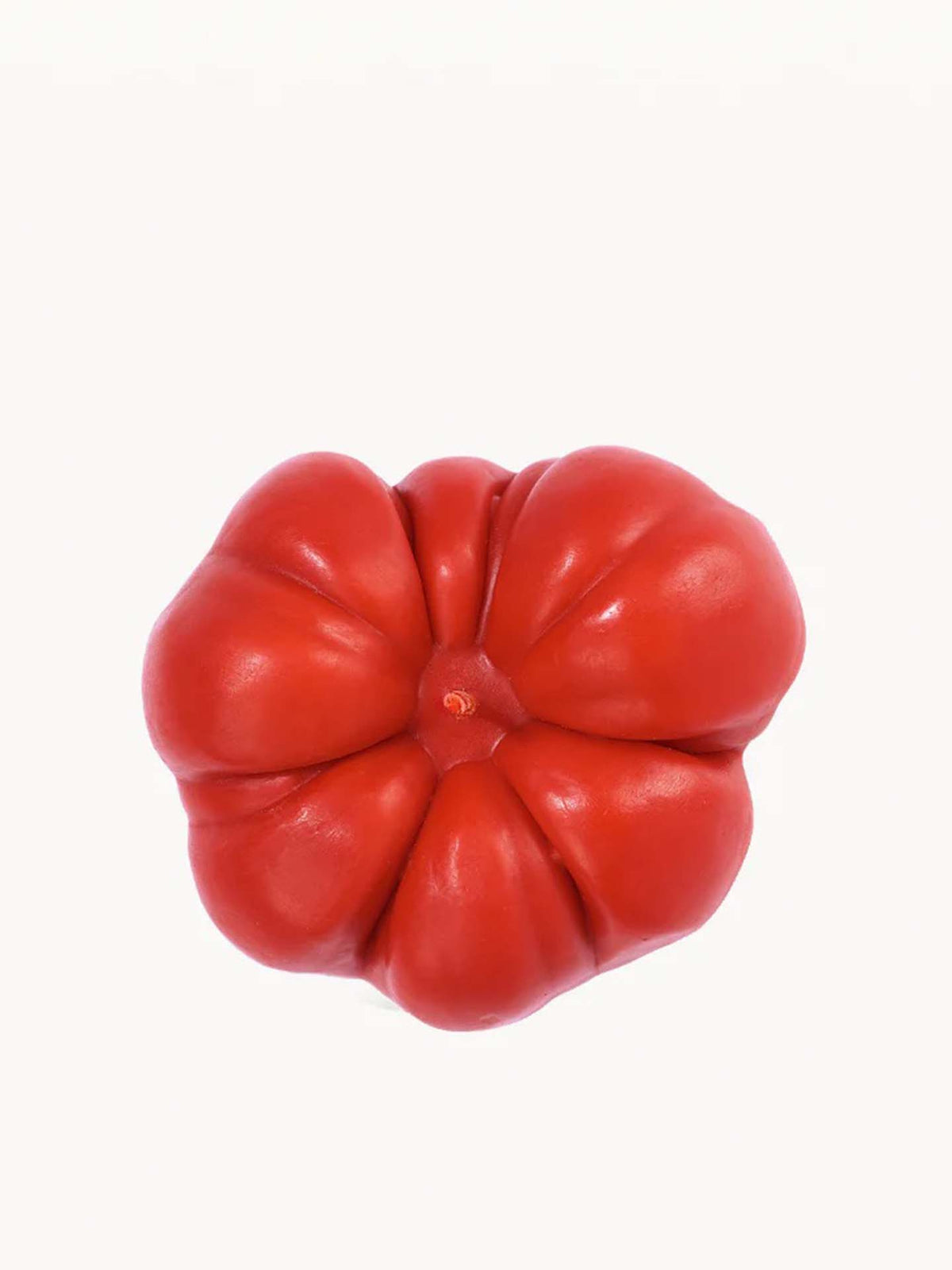 A hand-made, red Scented Tomato Candle from Nonna&#39;s Grocer, featuring a bumpy surface, stands out against a plain white background, reminiscent of a finely crafted bell pepper.