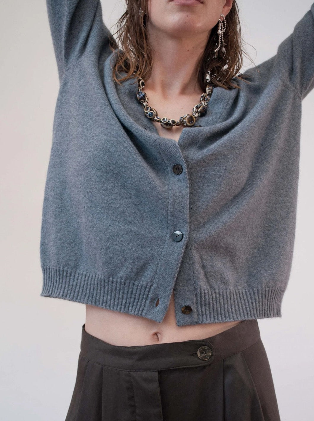 A woman wearing a Kom Cardigan – Stone by OVNA OVICH and black pants.