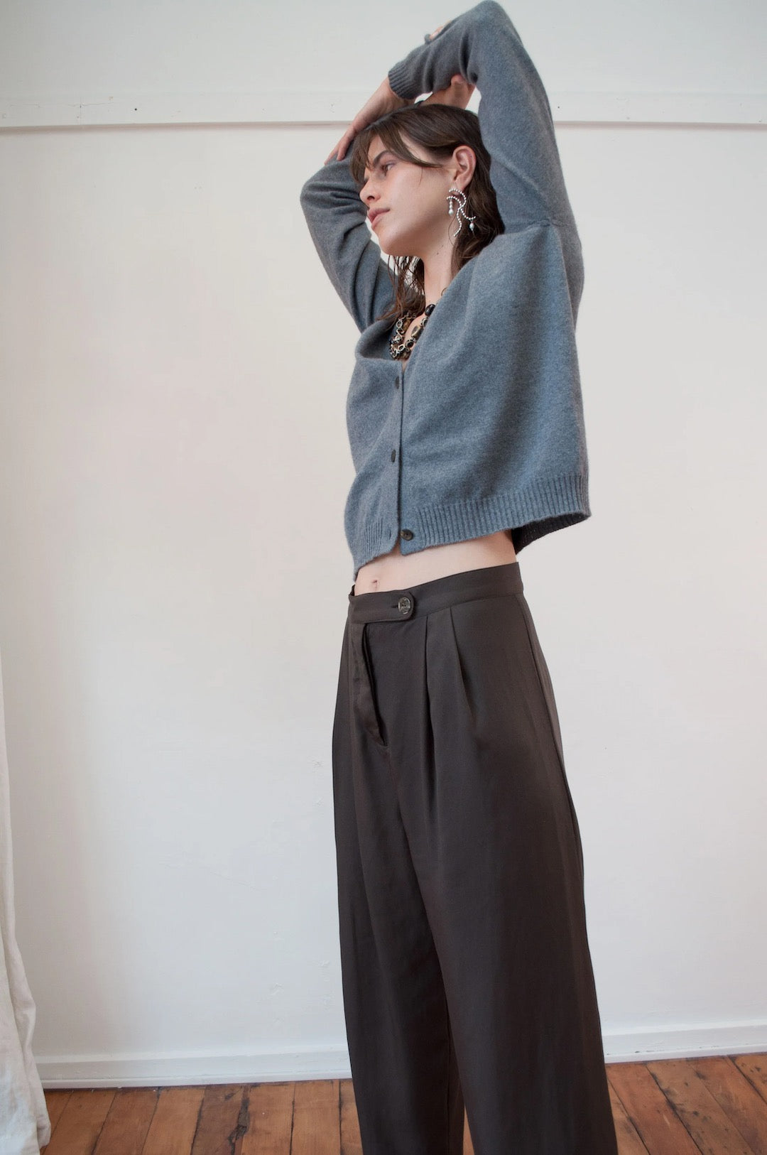 A woman is standing in a room wearing an OVNA OVICH Kom Cardigan - Stone and wide leg pants.