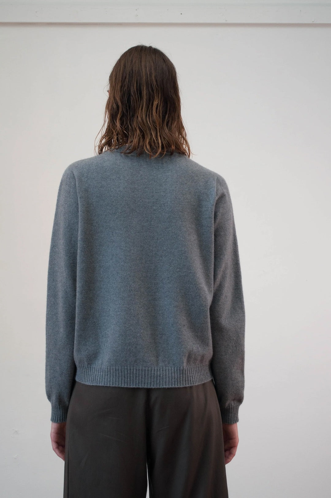 The back view of a woman wearing the OVNA OVICH Kom Cardigan - Stone and trousers.