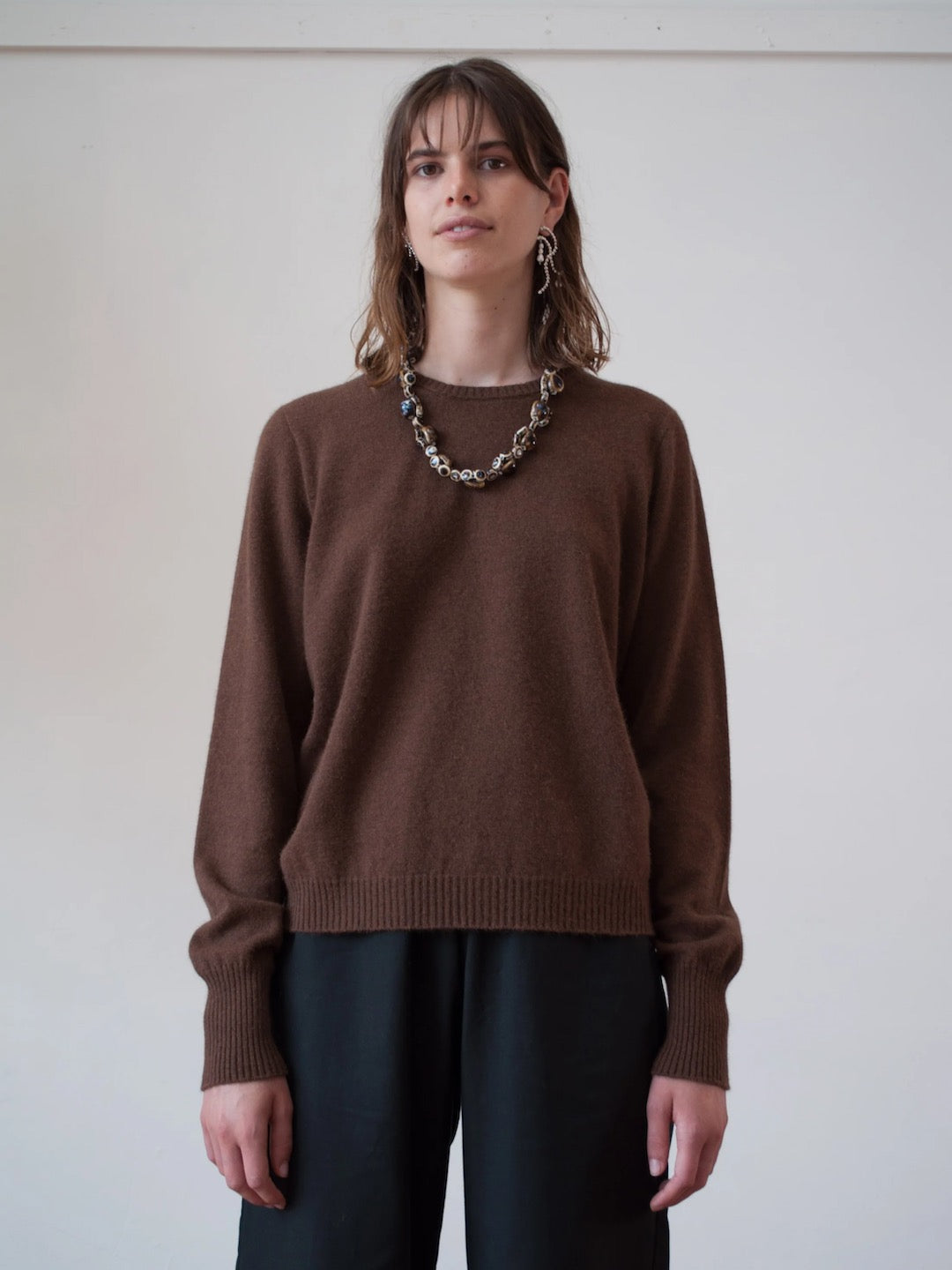 The model is wearing a OVNA OVICH Kom Jumper – Mud and black pants.