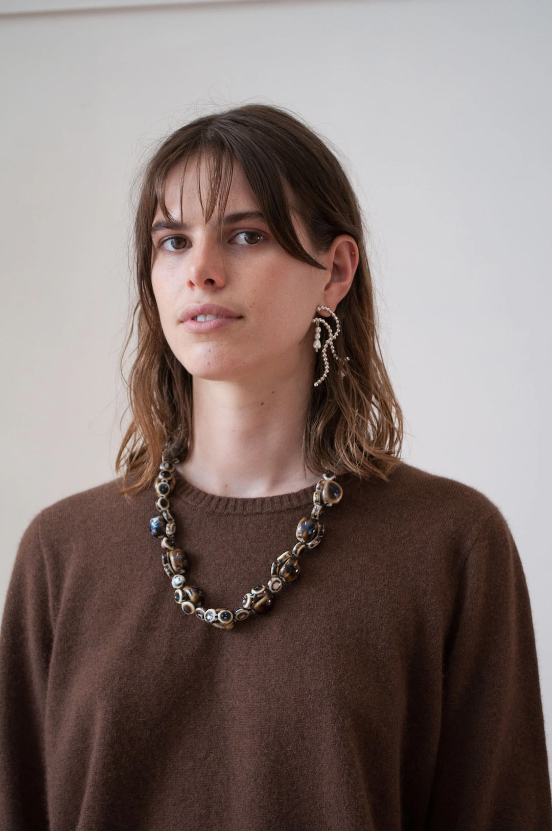 A woman wearing a OVNA OVICH Kom Jumper – Mud sweater and necklace.