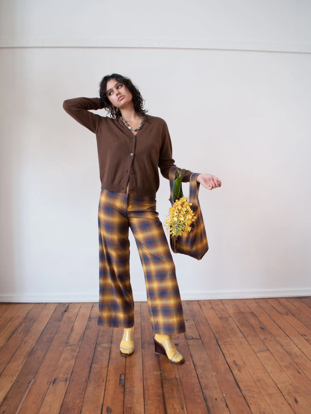 A woman in yellow and brown plaid pants holding a bouquet of Wander Bag – Sun Plaid (Pre-order) flowers, by OVNA OVICH.