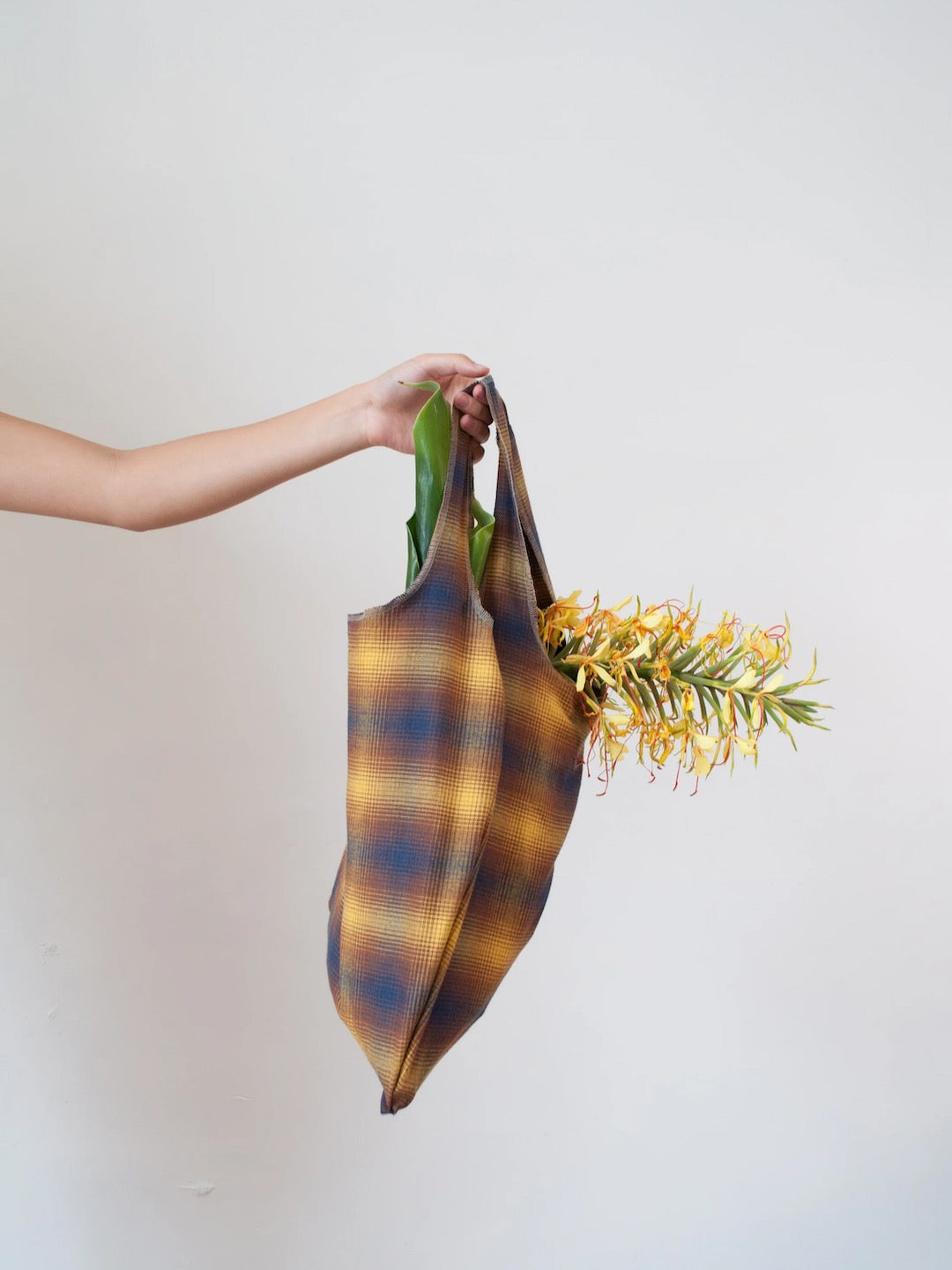 A woman holding a Wander Bag – Sun Plaid (Pre-order) by OVNA OVICH.