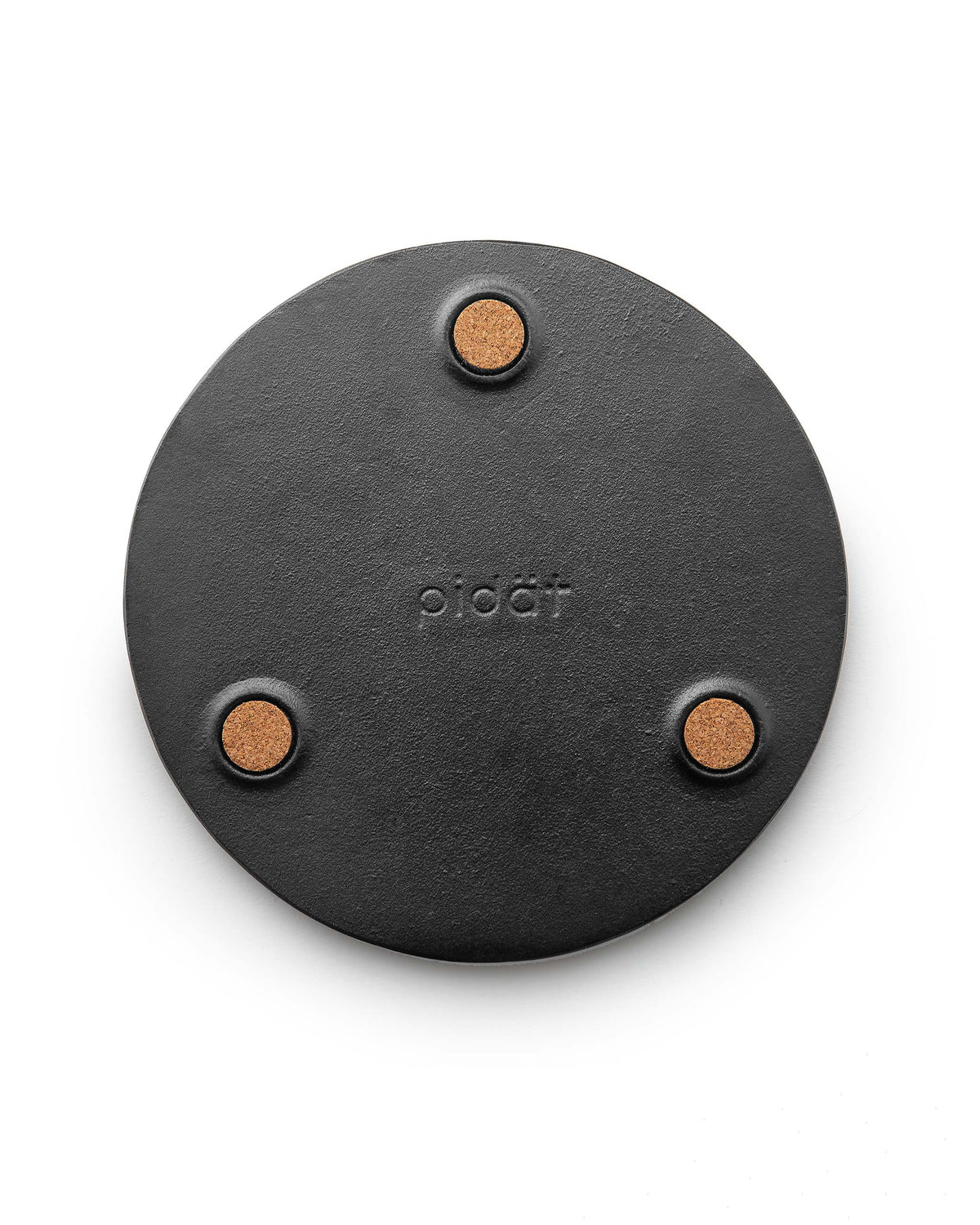 A round black trivet with the brand name “pidät” embossed in the center and three circular cork feet on the underside.