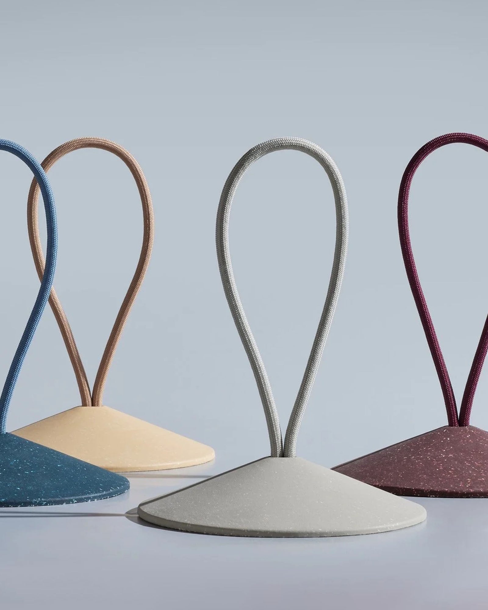 A door is held open by a minimalist, gray wedge-shaped doorstop with a loop handle, placed on a light floor next to a muted mauve door.
