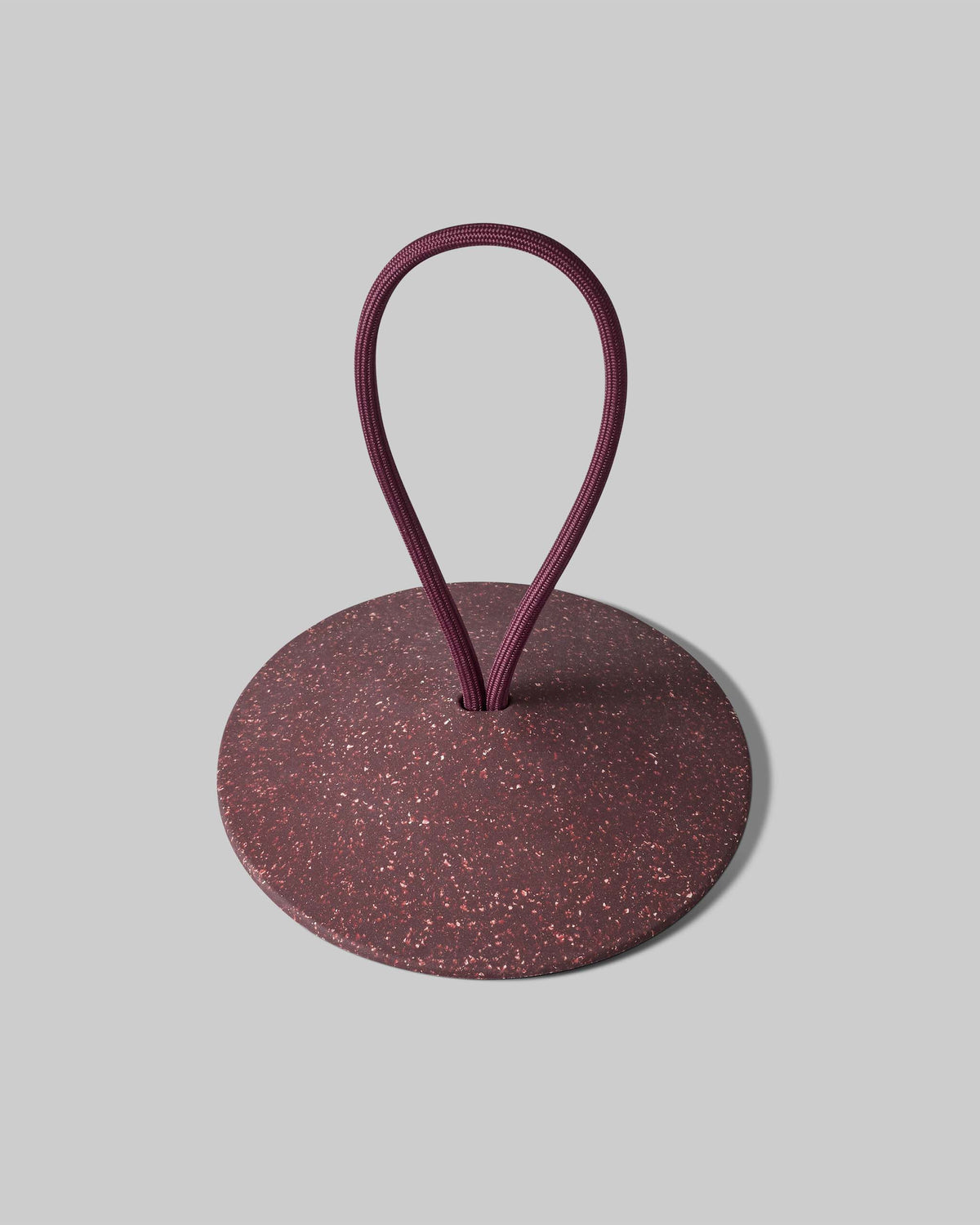 A round, speckled maroon object with a flat base and a looped cord emerging from the center, displayed on a plain gray background.