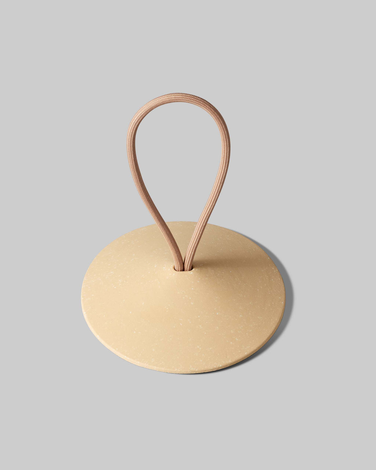 Beige circular object with a tan elastic loop attached at the center, placed on a plain gray background.