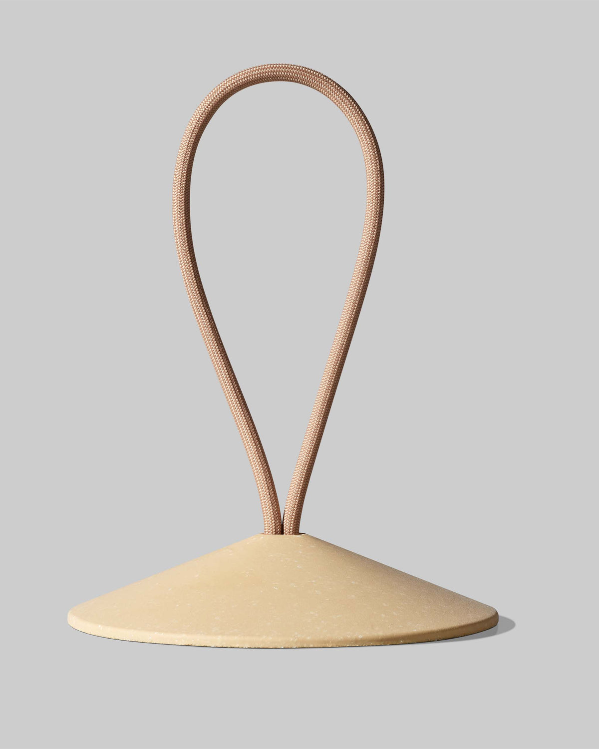 A beige, cone-shaped object with a brown looped cord emerging from its top sits against a plain gray background.