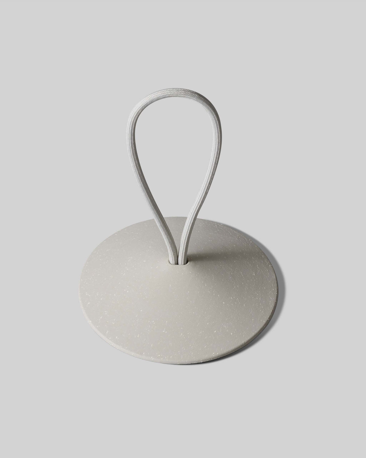 A round, flat, gray object with a looped white cord emerging from its center, placed on a light gray background.
