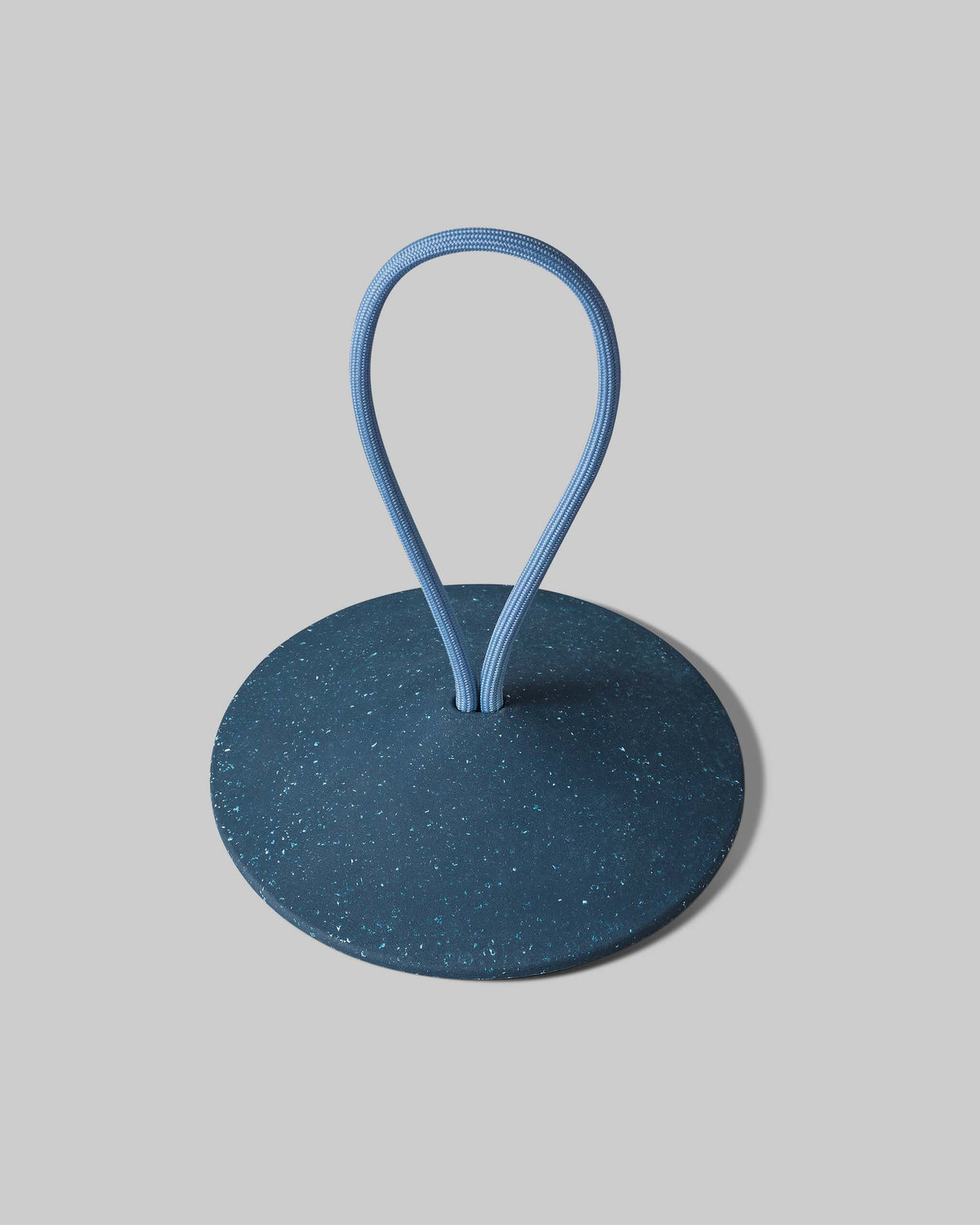 A round, dark blue speckled object with a circular base and a blue flexible loop extending from its center, set against a plain light gray background.