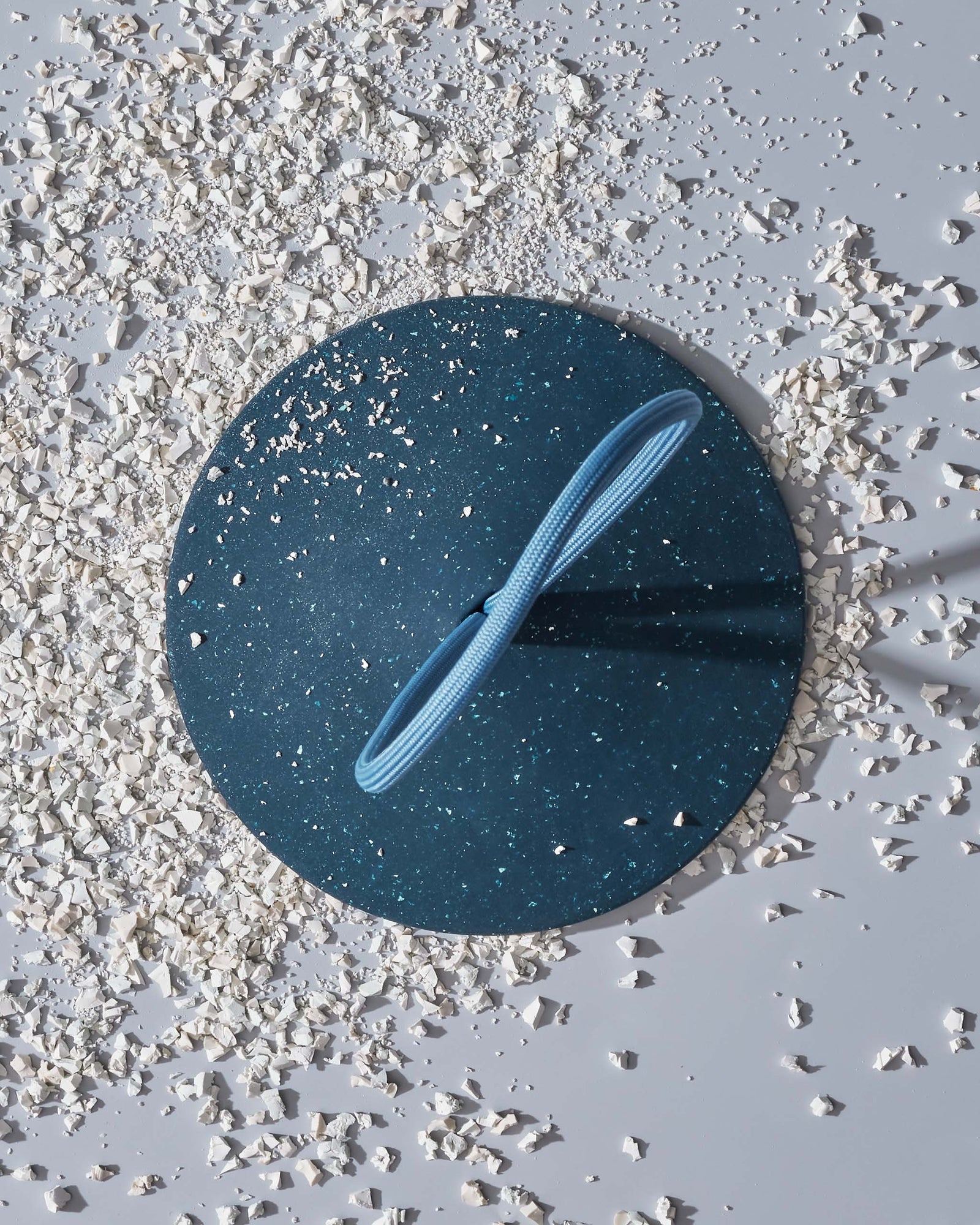 A round blue doorstop with a looped handle holds open a beige door on a light blue tiled floor.