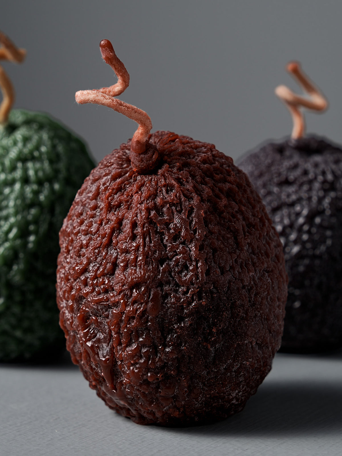 The Dark Green Avocado Candle showcases New Zealand handmade artistry with its textured, oval shape and twisted wick—standing out in deep green against a neutral backdrop.