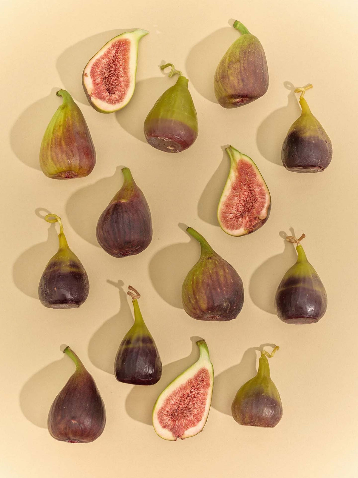Whole and halved figs are arranged on a beige background in a neat, evenly spaced pattern, reflecting the attention to detail in creating the Fig Candle.