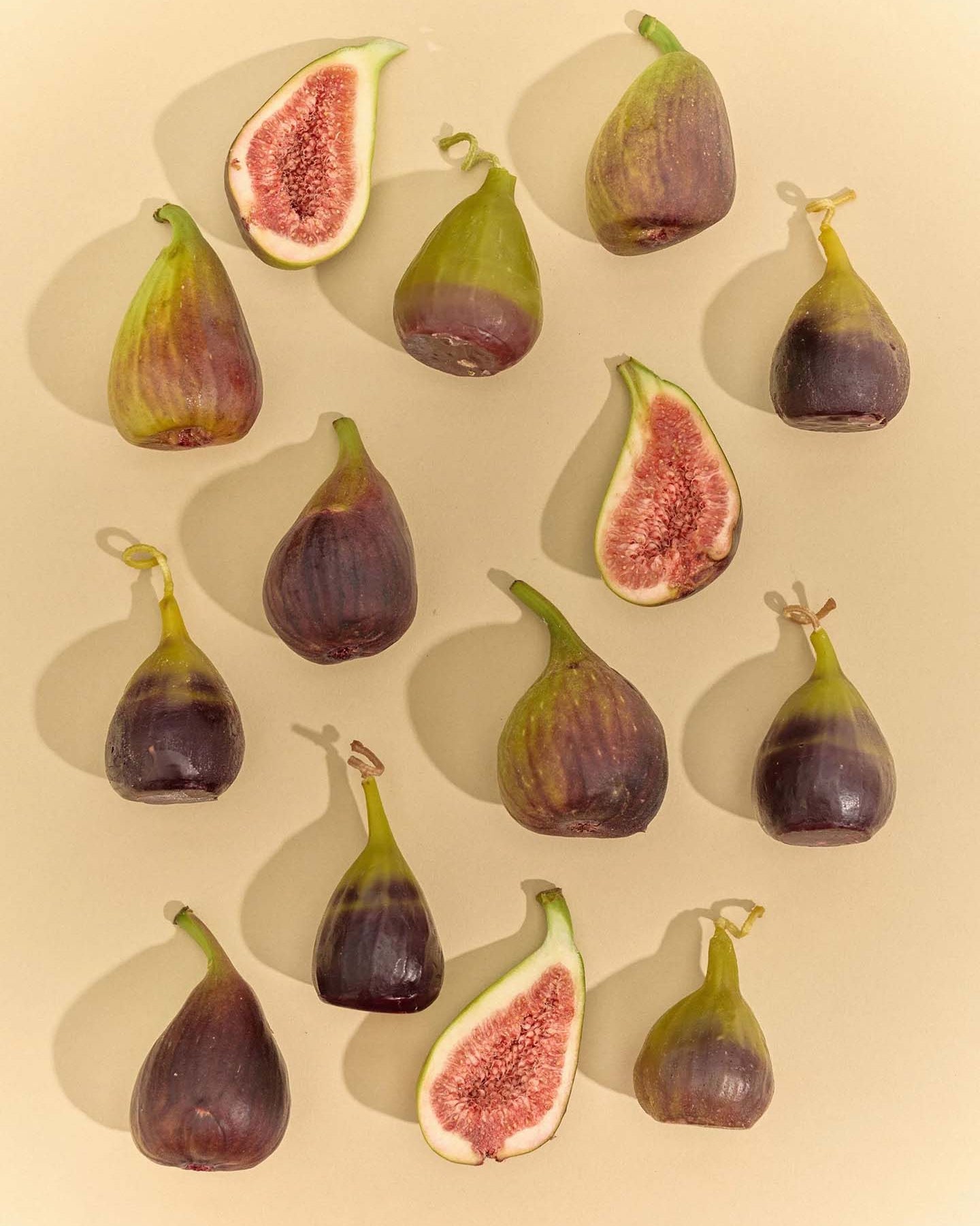 The Fig Candle, featuring a purple base and green top, stands upright on a light gray surface against a plain gray background, resembling a real fig.