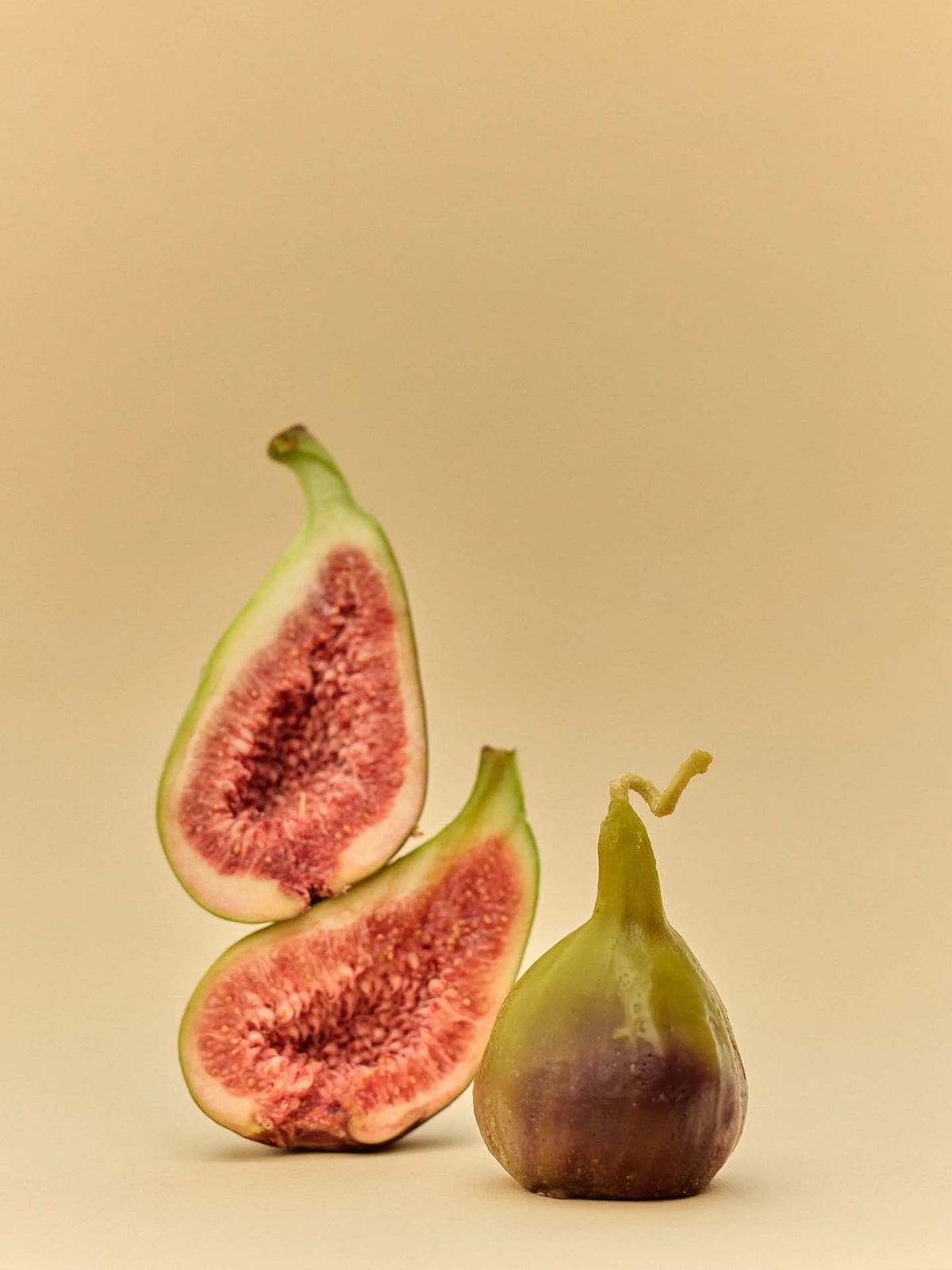 A whole fig and two fig halves are shown on a plain beige background, echoing the natural hues of the Fig Candle.