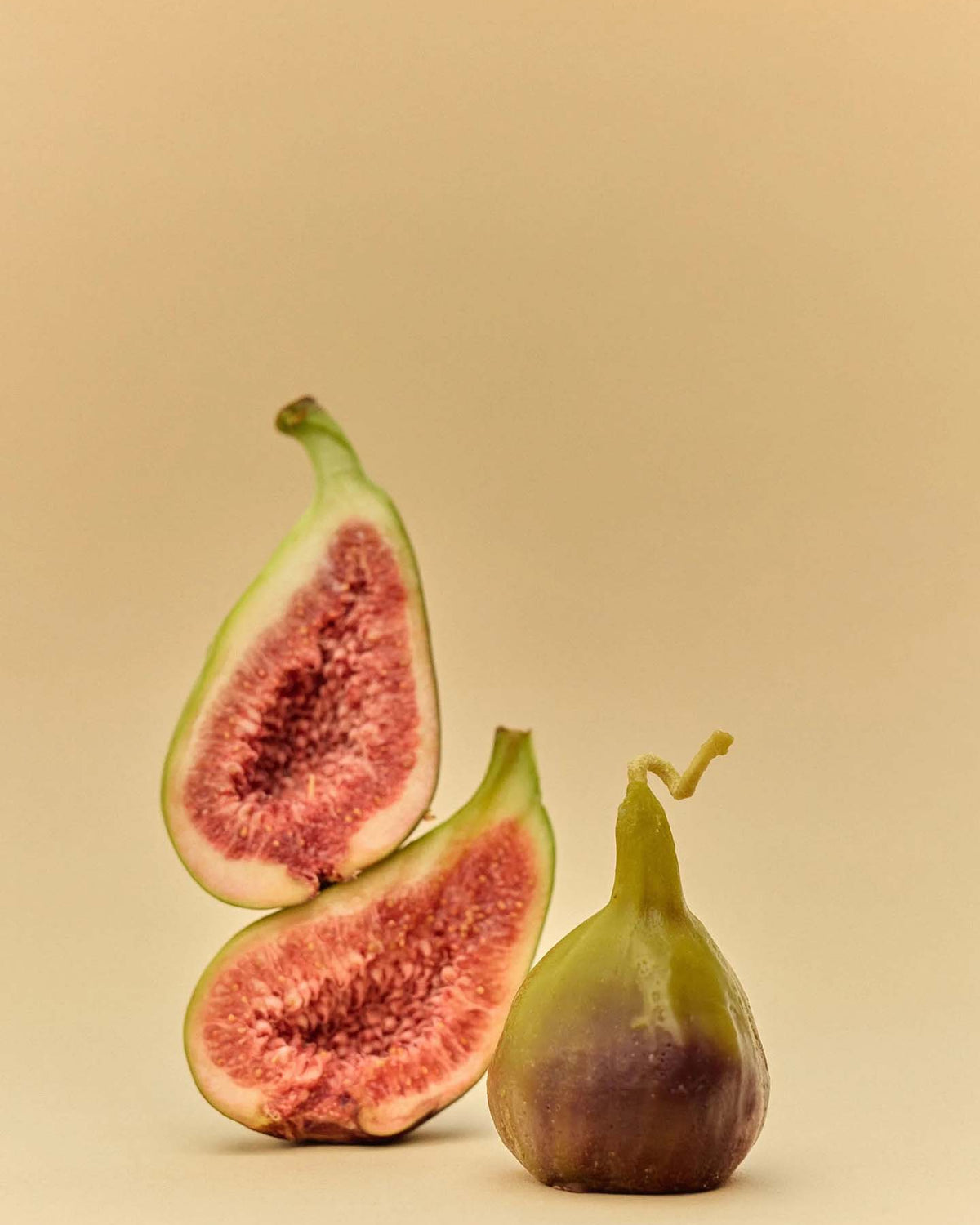 A whole fig and two fig halves are shown on a plain beige background, echoing the natural hues of the Fig Candle.