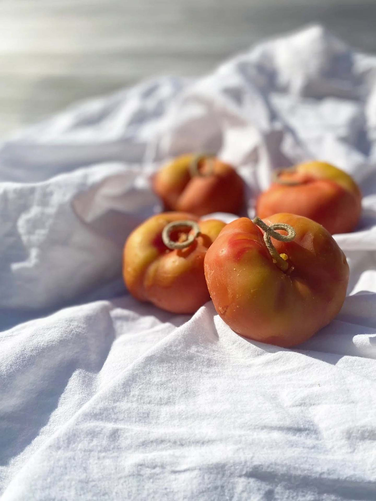 Four heirloom tomatoes sit on a white cloth in natural sunlight next to our Flat Peach Candle, a handmade New Zealand candle crafted from pure beeswax.