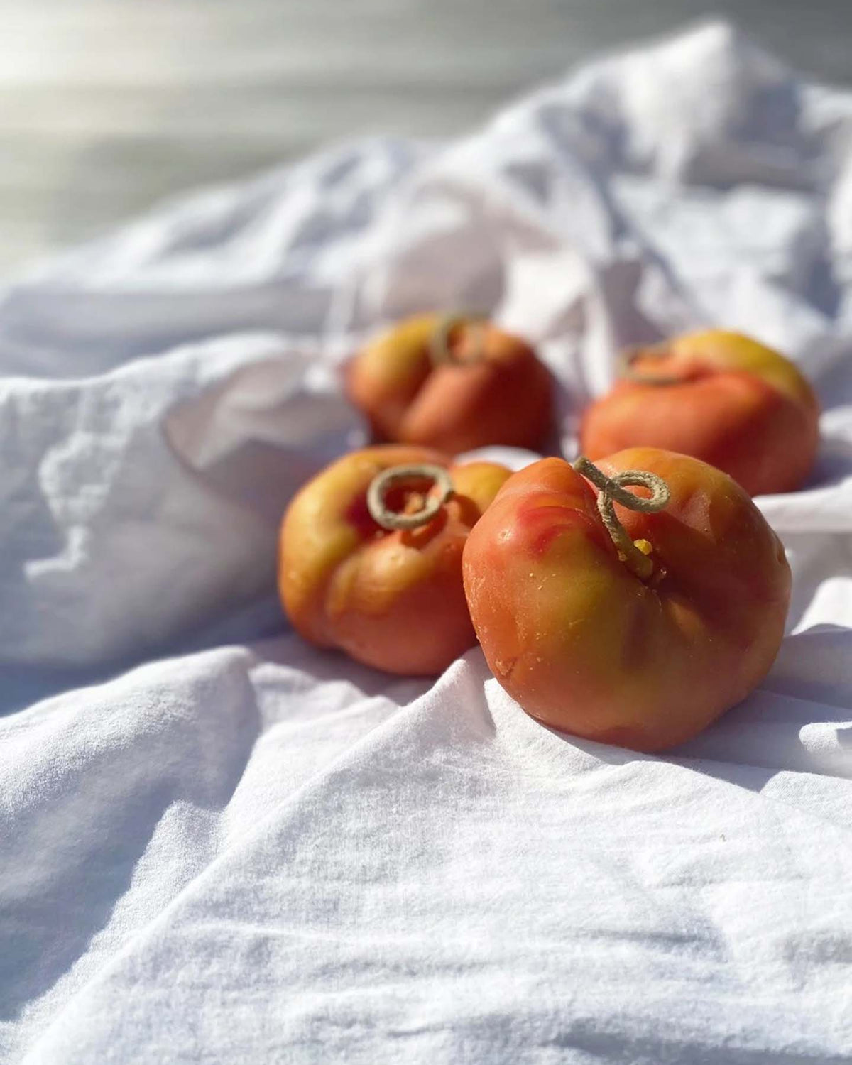 Four heirloom tomatoes sit on a white cloth in natural sunlight next to our Flat Peach Candle, a handmade New Zealand candle crafted from pure beeswax.