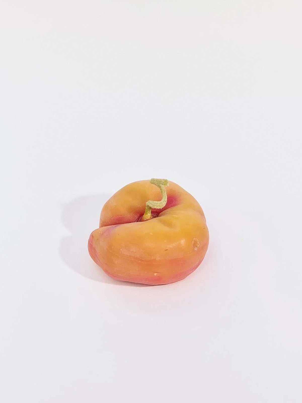 The Flat Peach Candle, featuring unique orange and red tones with a small stem, sits on a plain white surface.