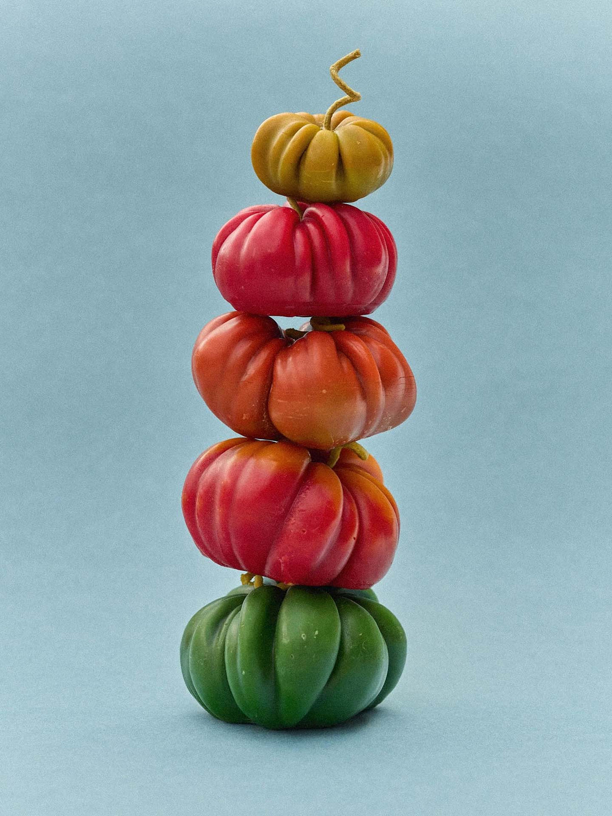 An Orange Heirloom Tomato Candle – Small sits on a plain light blue background, its vibrant shape and color resembling a playful handmade display.