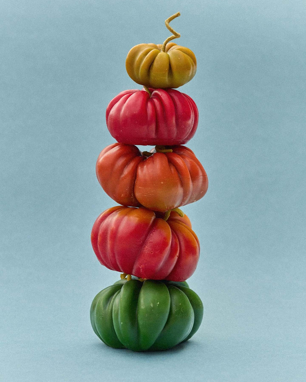 An Orange Heirloom Tomato Candle – Small sits on a plain light blue background, its vibrant shape and color resembling a playful handmade display.