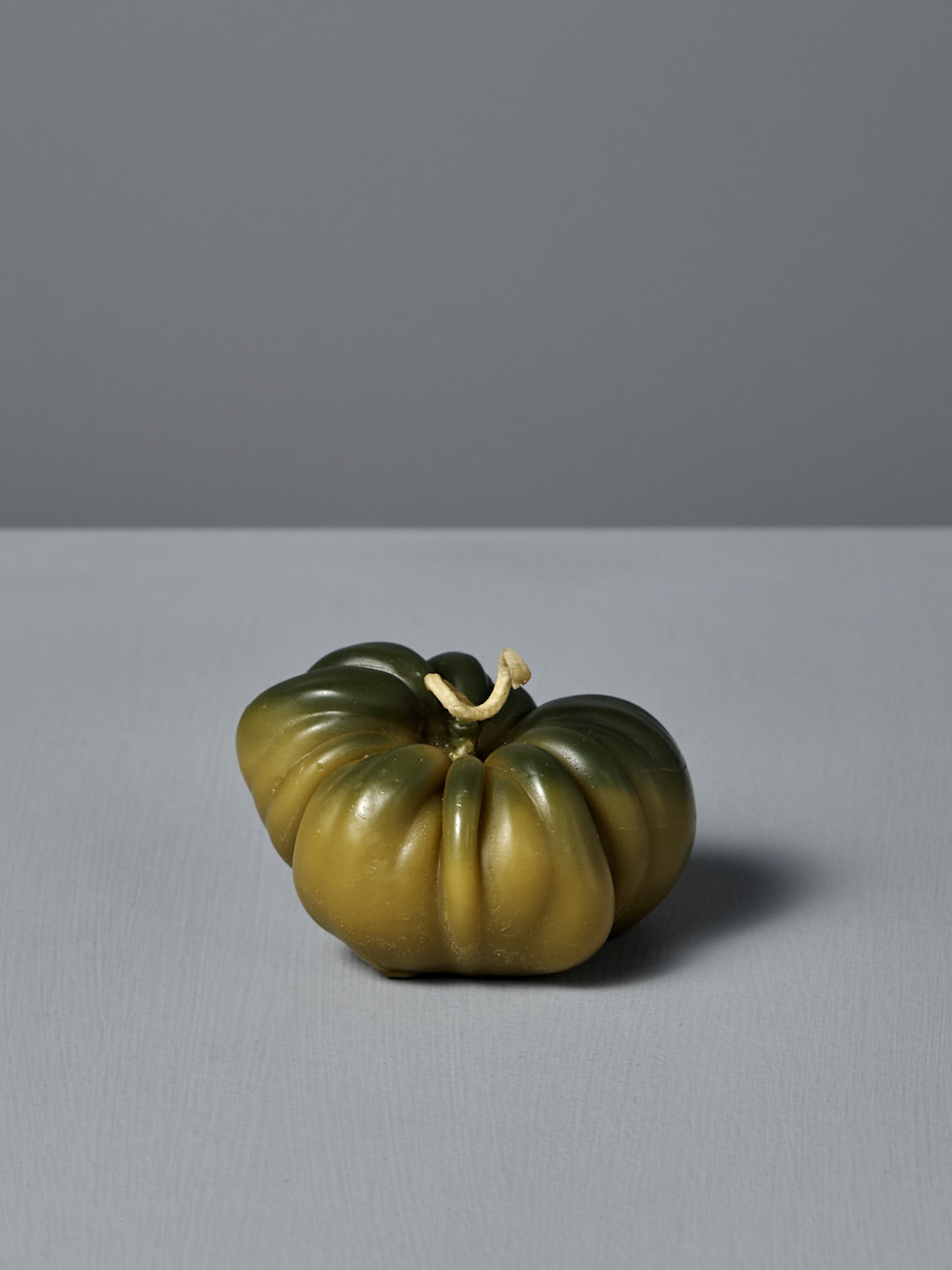 The Green Heirloom Tomato Candle – Large, handmade from pure New Zealand beeswax, with a short stem, sits on a light gray surface against a simple gray background.